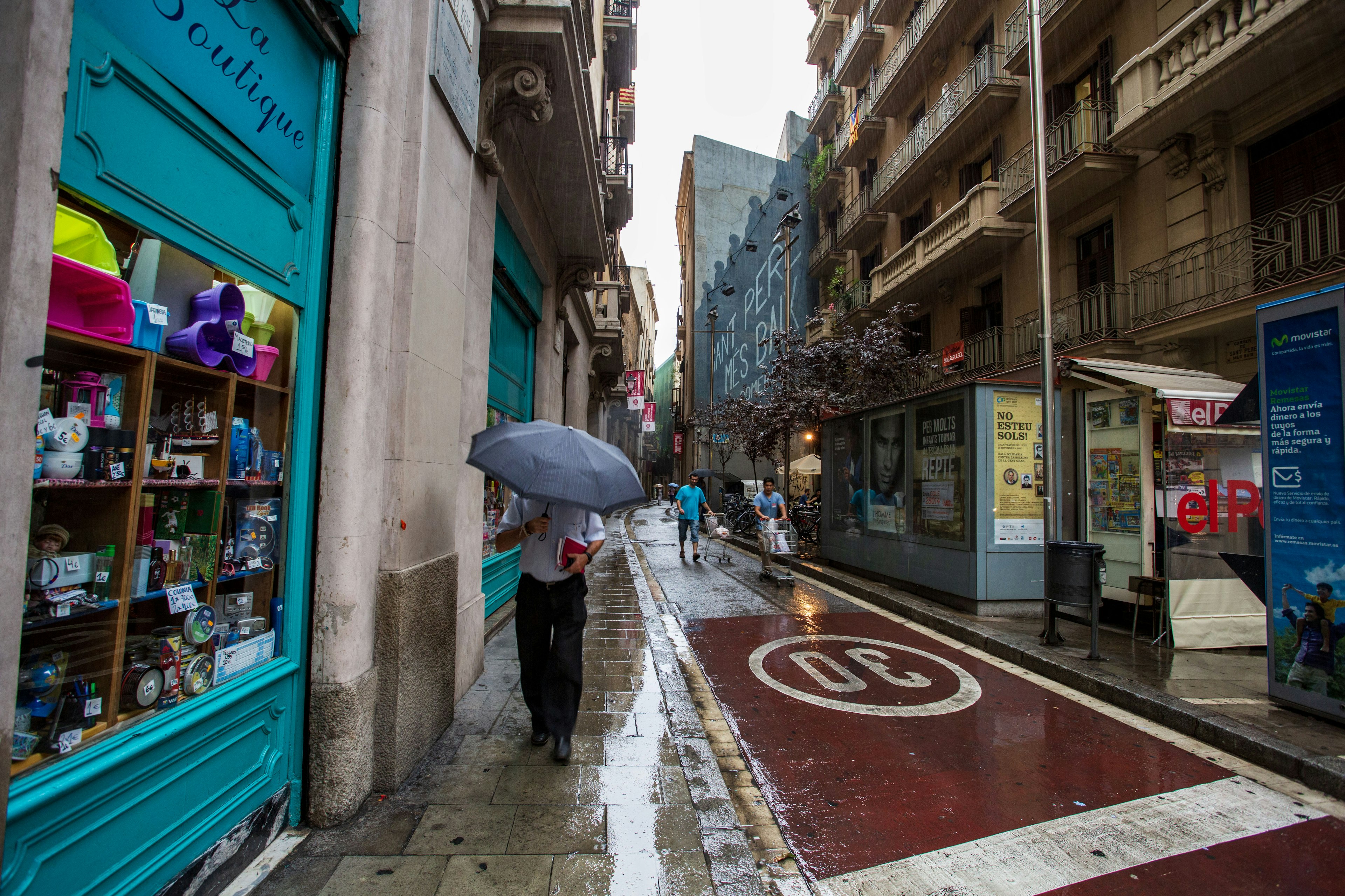 Una persona che cammina con un ombrello sotto la pioggia in una strada stretta con negozi colorati