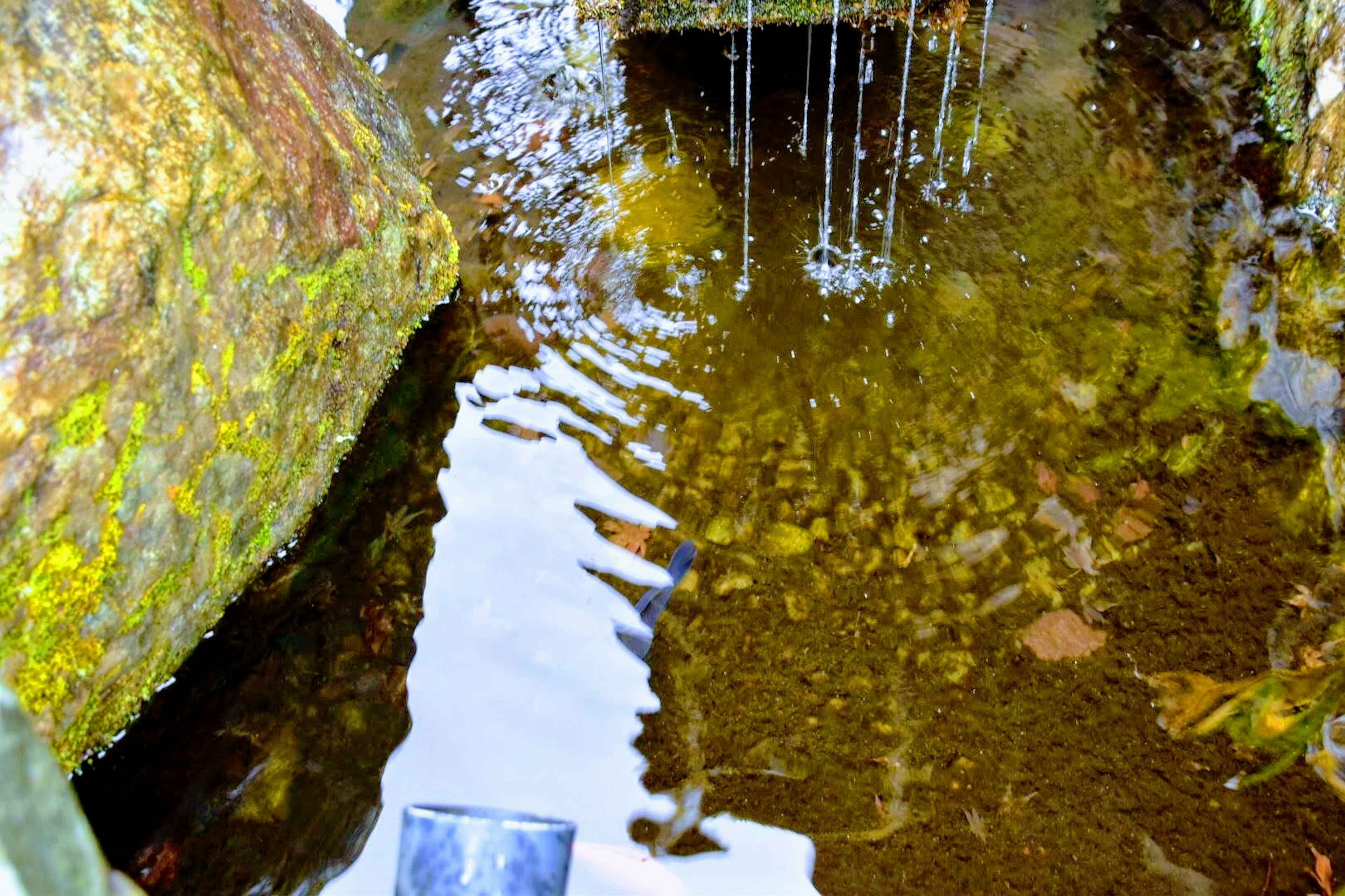 Image of a tranquil water surface reflecting rocks and water droplets