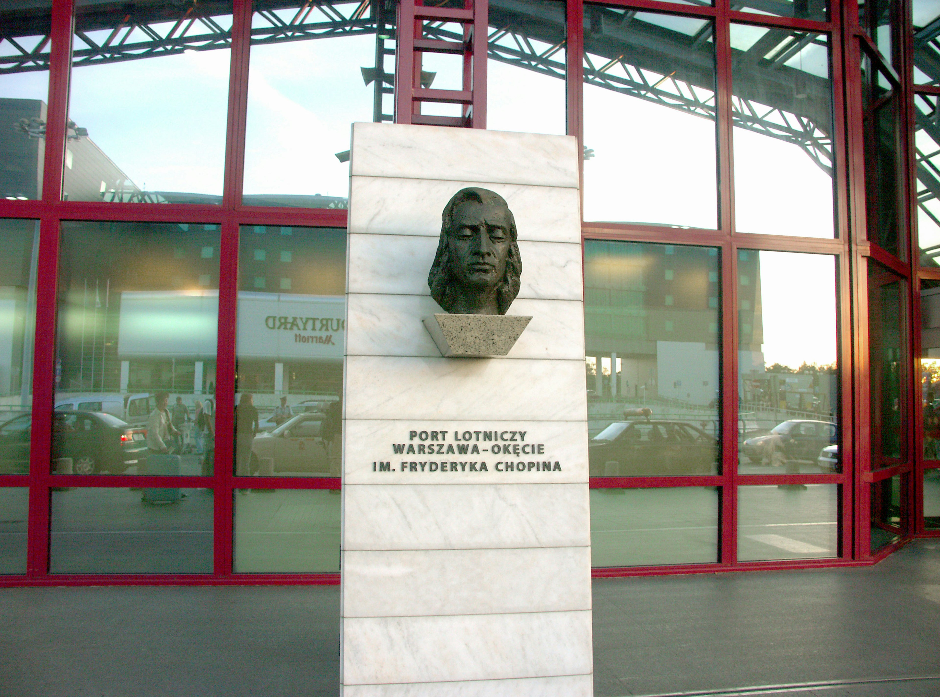 Columna de piedra con un busto esculpido y fachada de edificio de vidrio