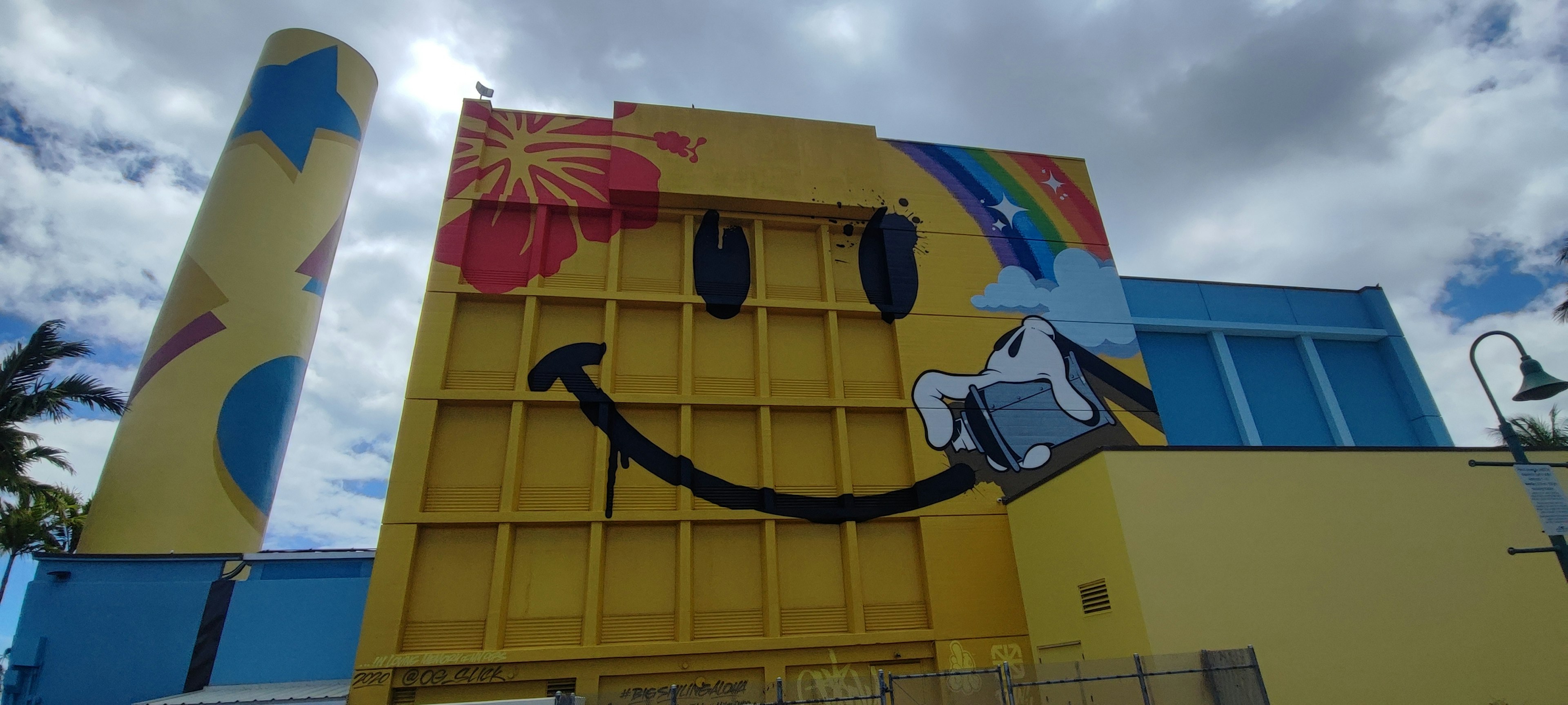 Große gelbe Wand mit einem lächelnden Gesicht und buntem Regenbogen