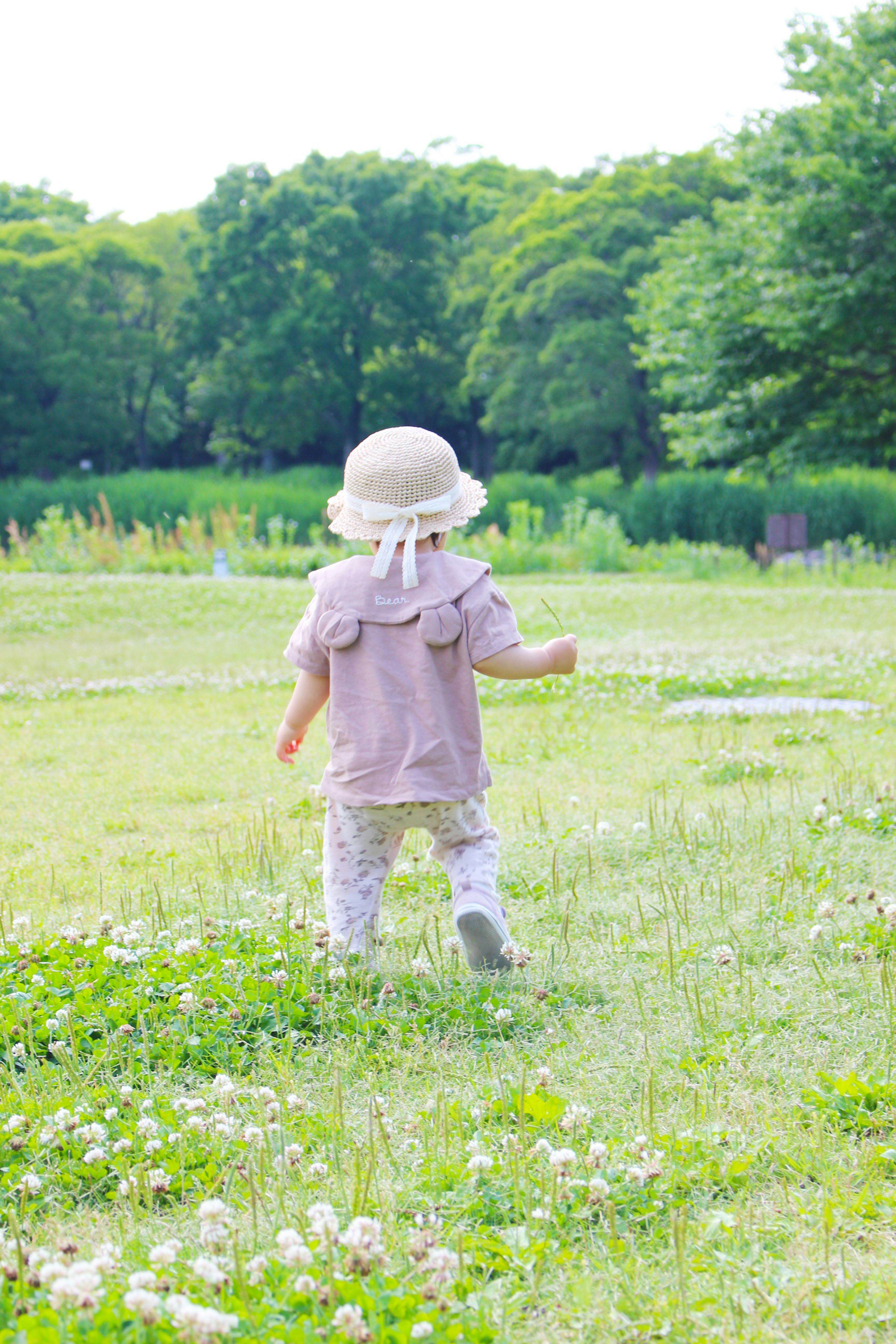 A child wearing a hat walks through a grassy field