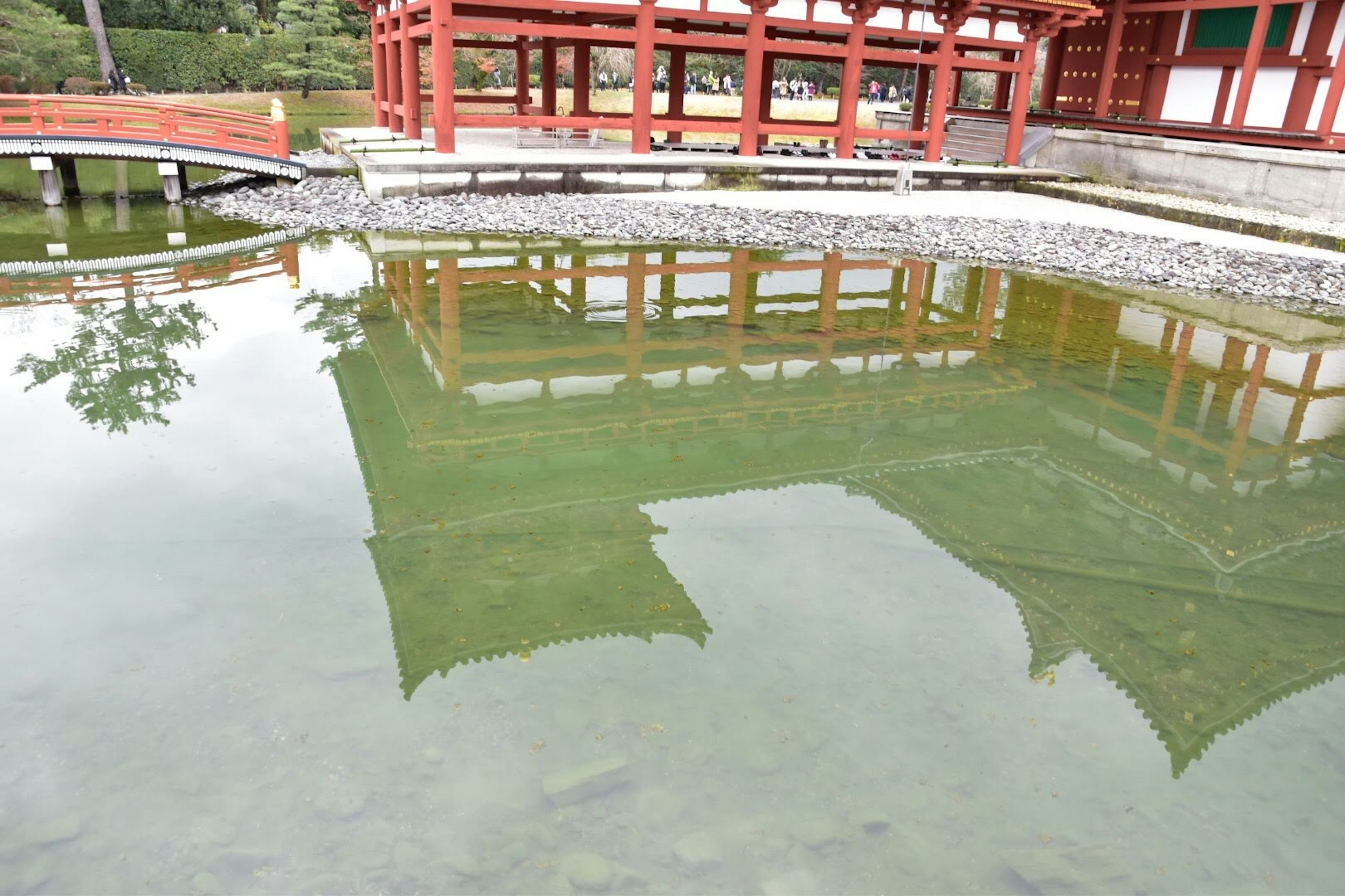 Refleksi bangunan merah di kolam tenang dikelilingi oleh vegetasi