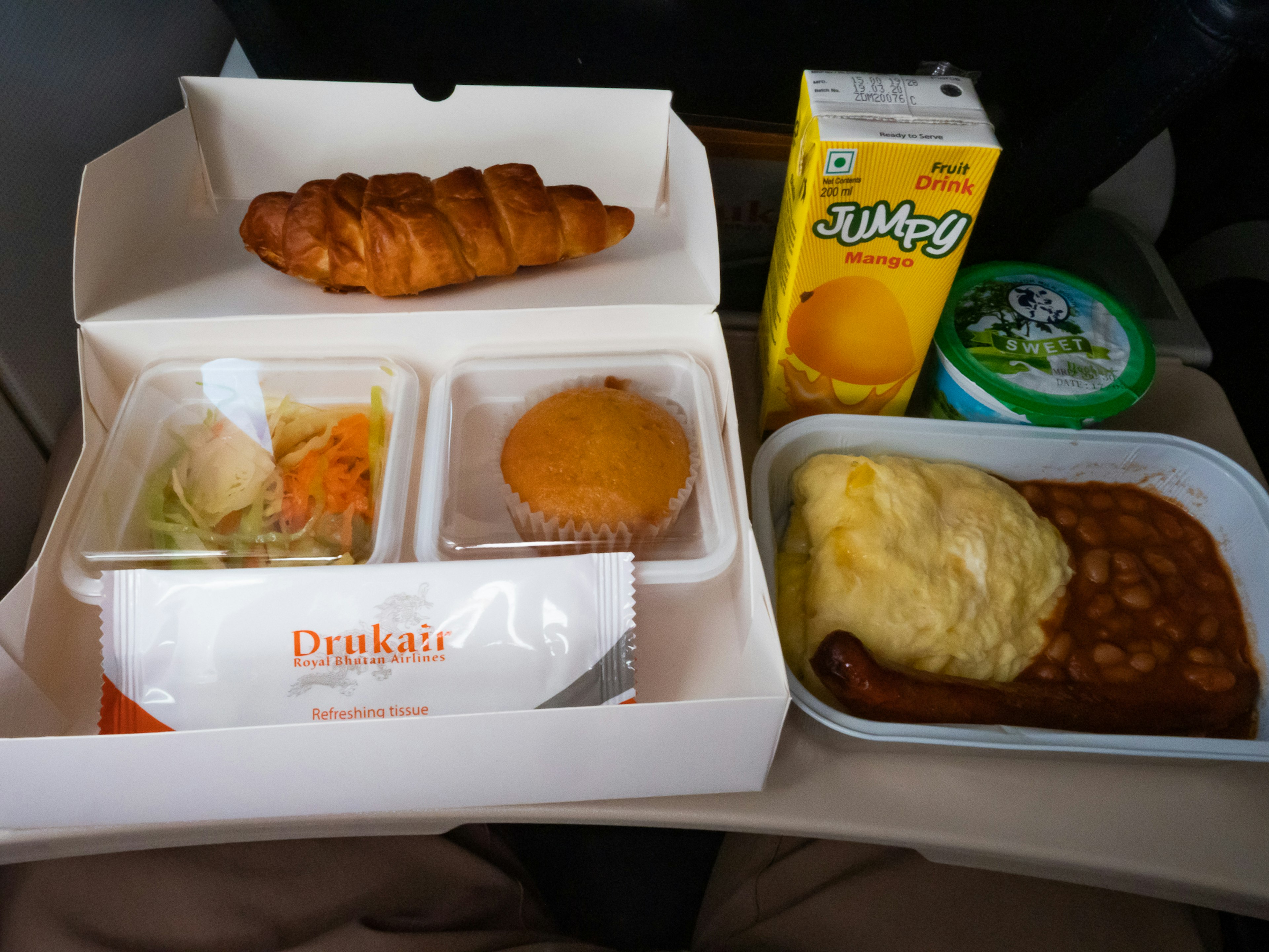 In-flight meal tray with salad, cupcake, omelette rice, sausage, and baked beans