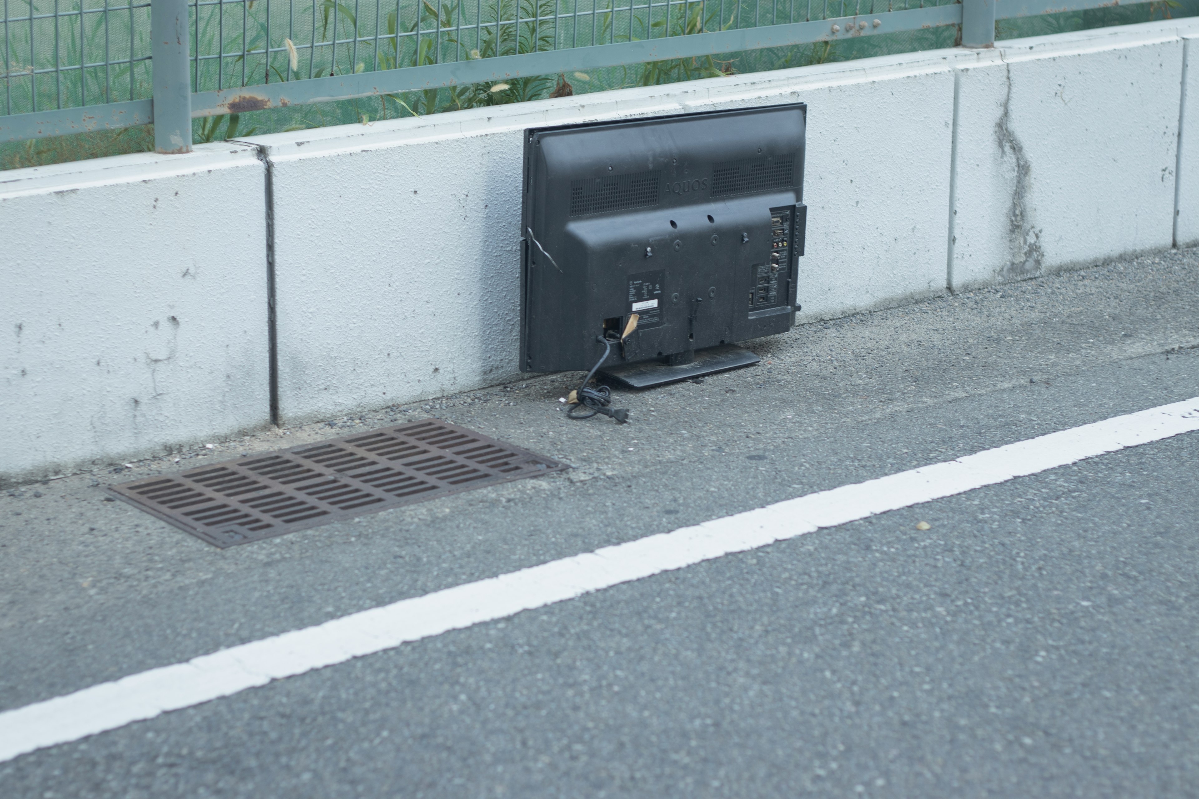 Une vieille télévision placée au bord de la route à côté d'une grille de drainage