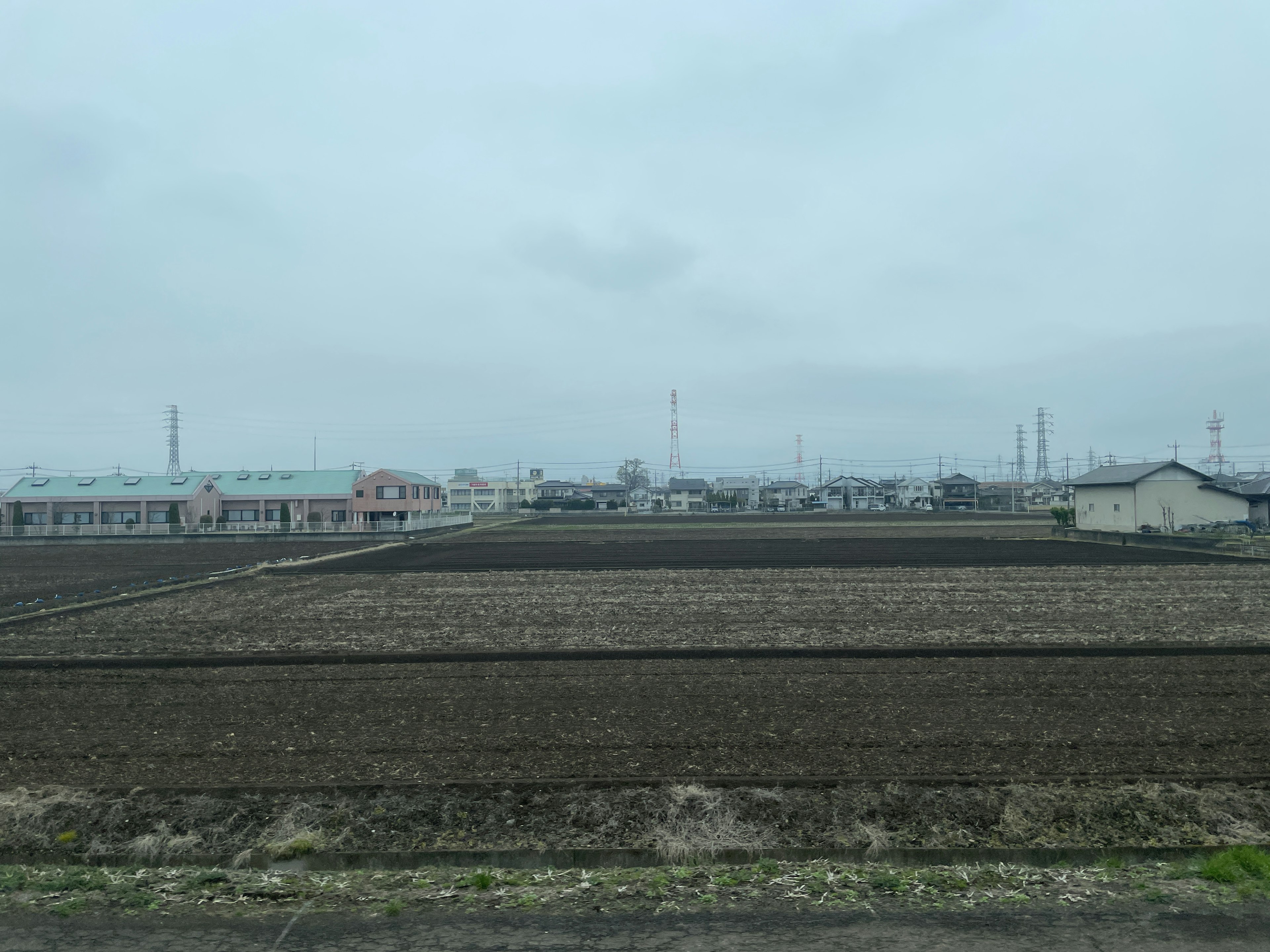 Landschaft mit landwirtschaftlichen Flächen und Häusern unter einem bewölkten Himmel