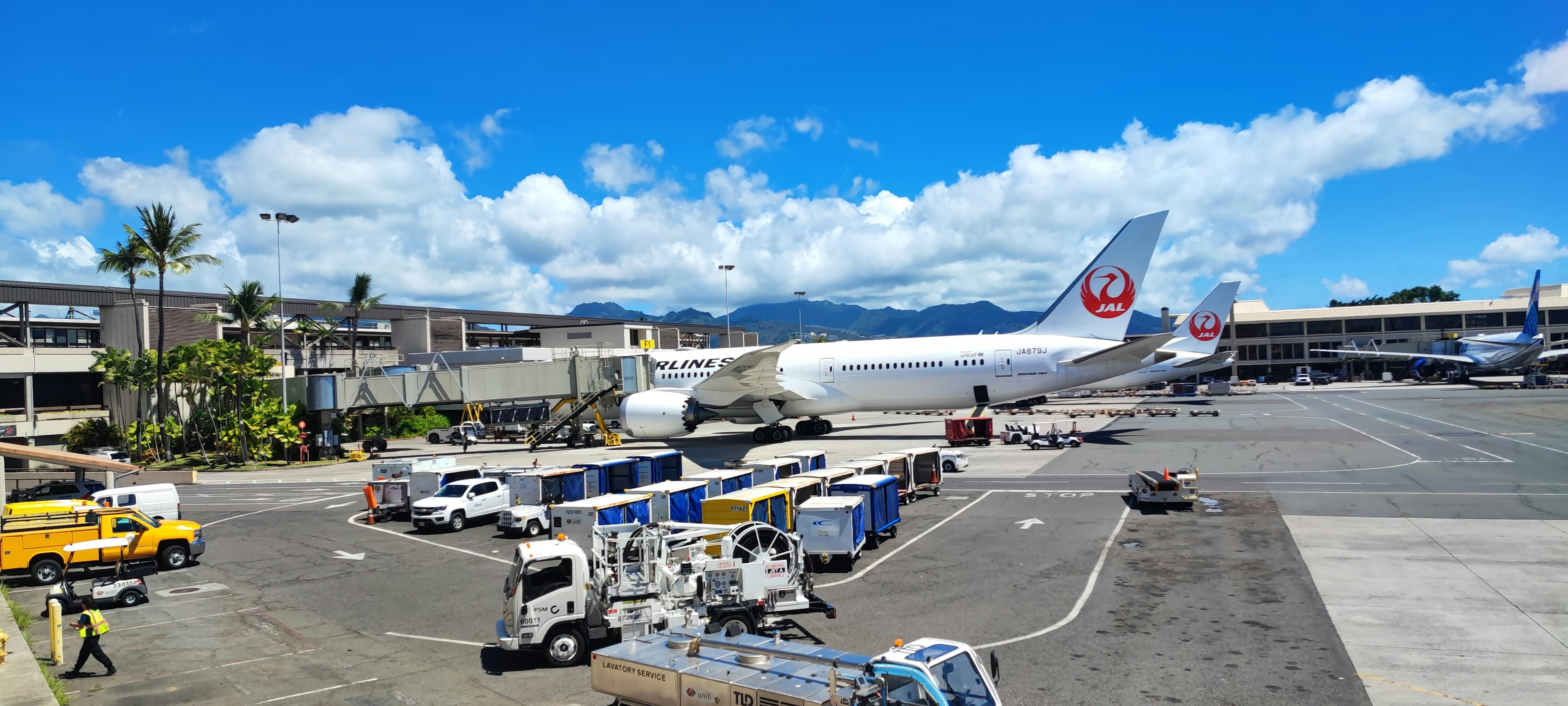 Airport scene featuring a Japan Airlines airplane and cargo trucks