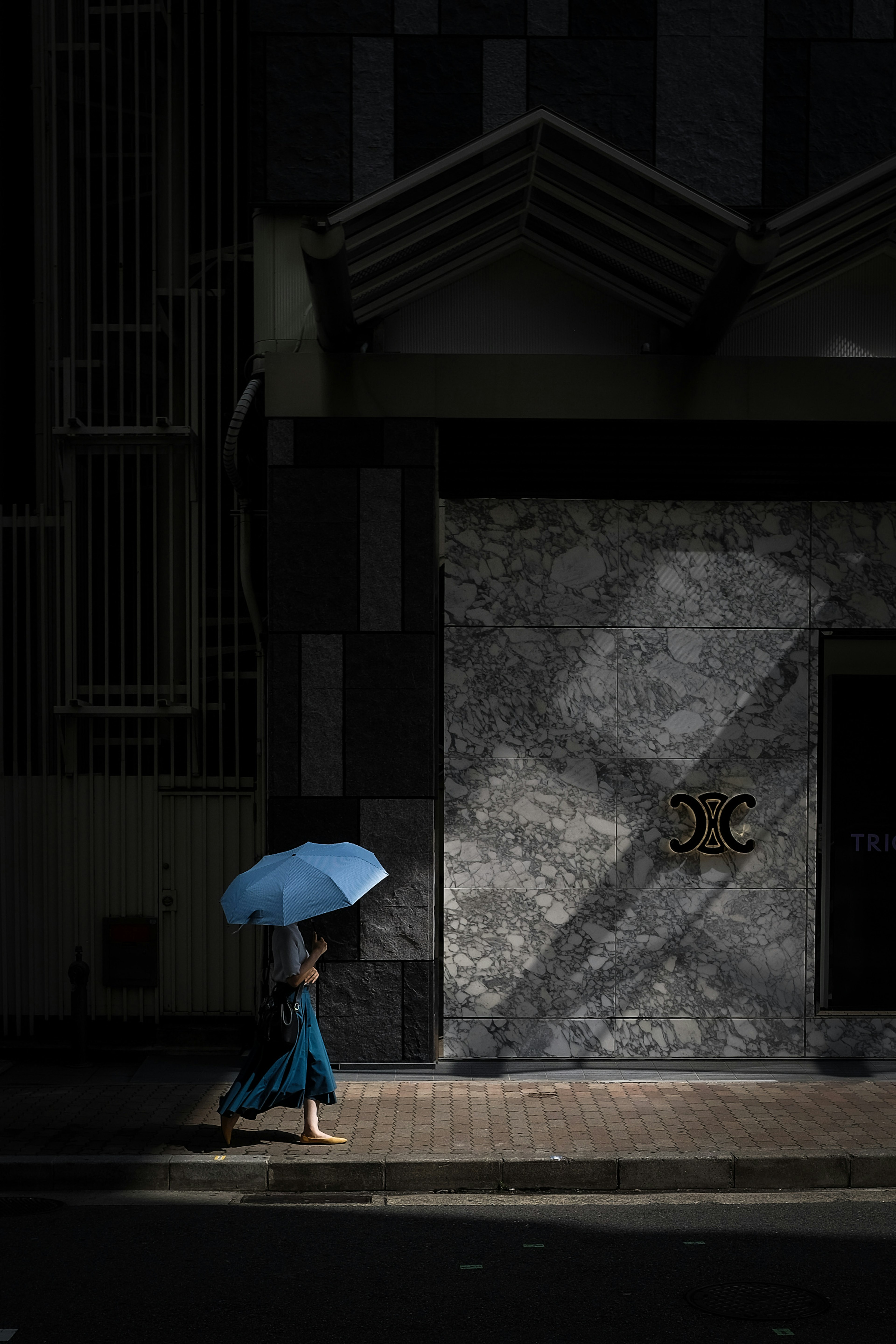 Frau, die mit einem blauen Regenschirm auf einer dunklen Straße geht