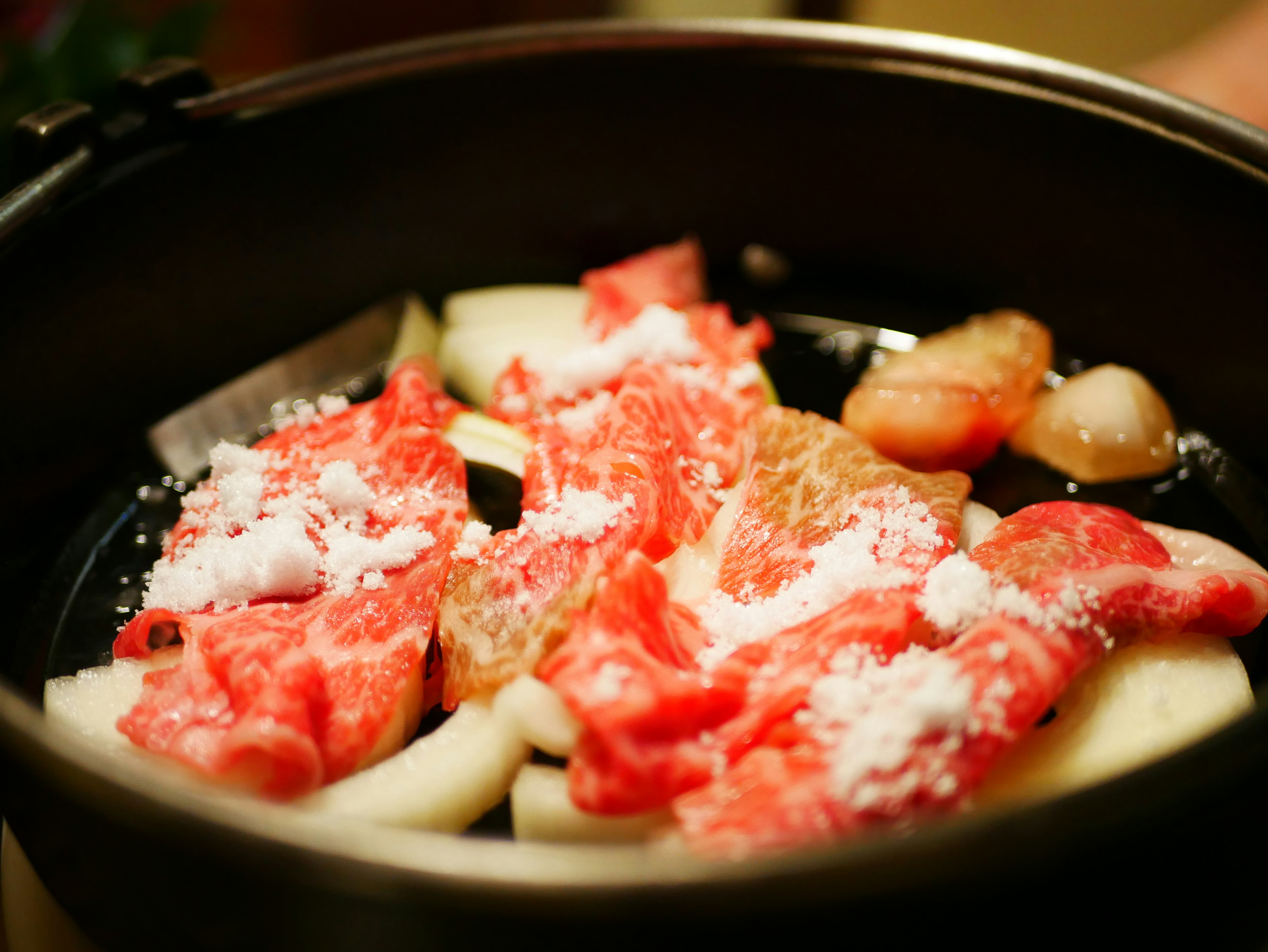 A pot filled with sliced meat and vegetables garnished with salt