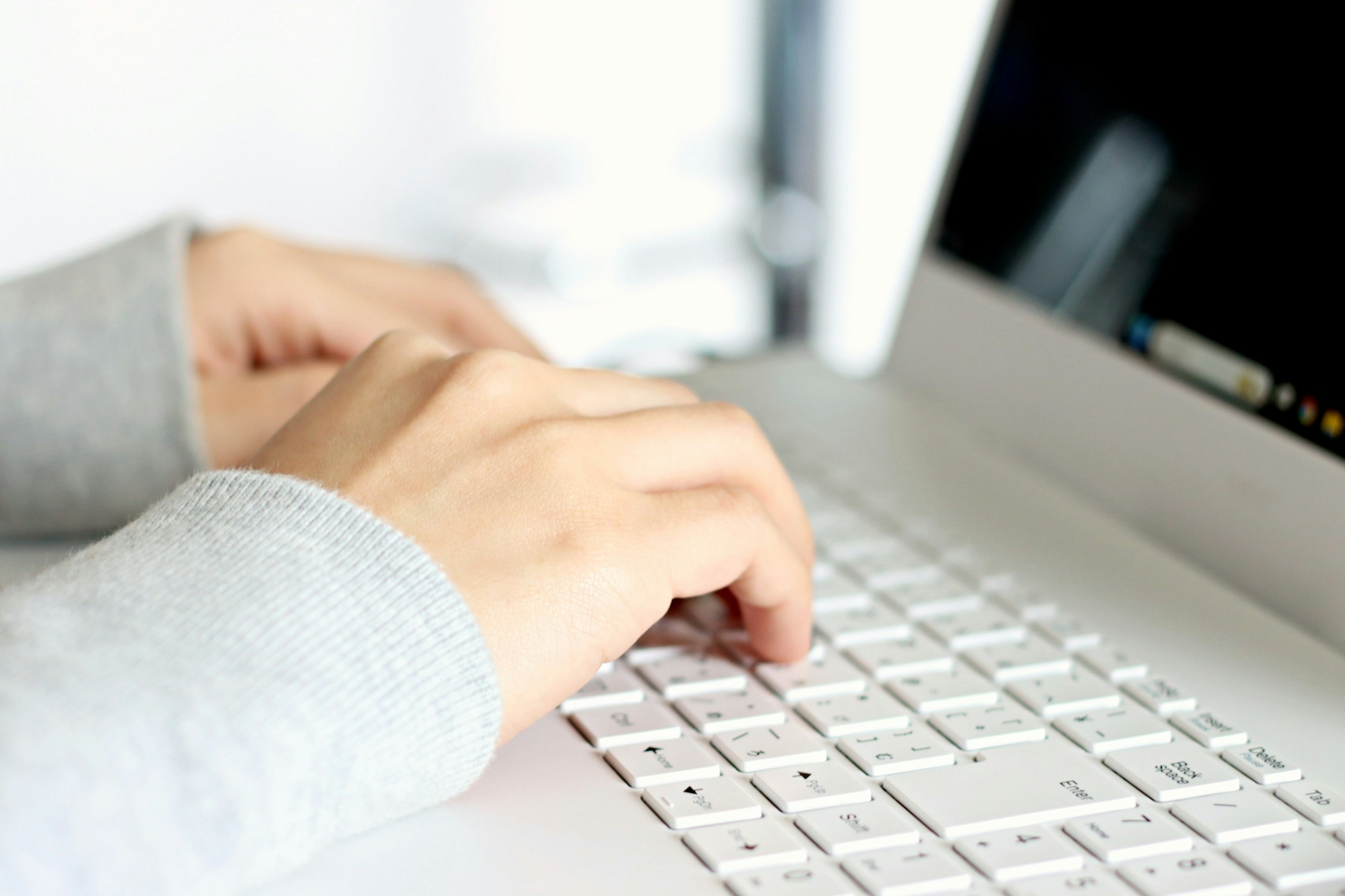 Mains portant un pull gris tapant sur le clavier d'un ordinateur portable