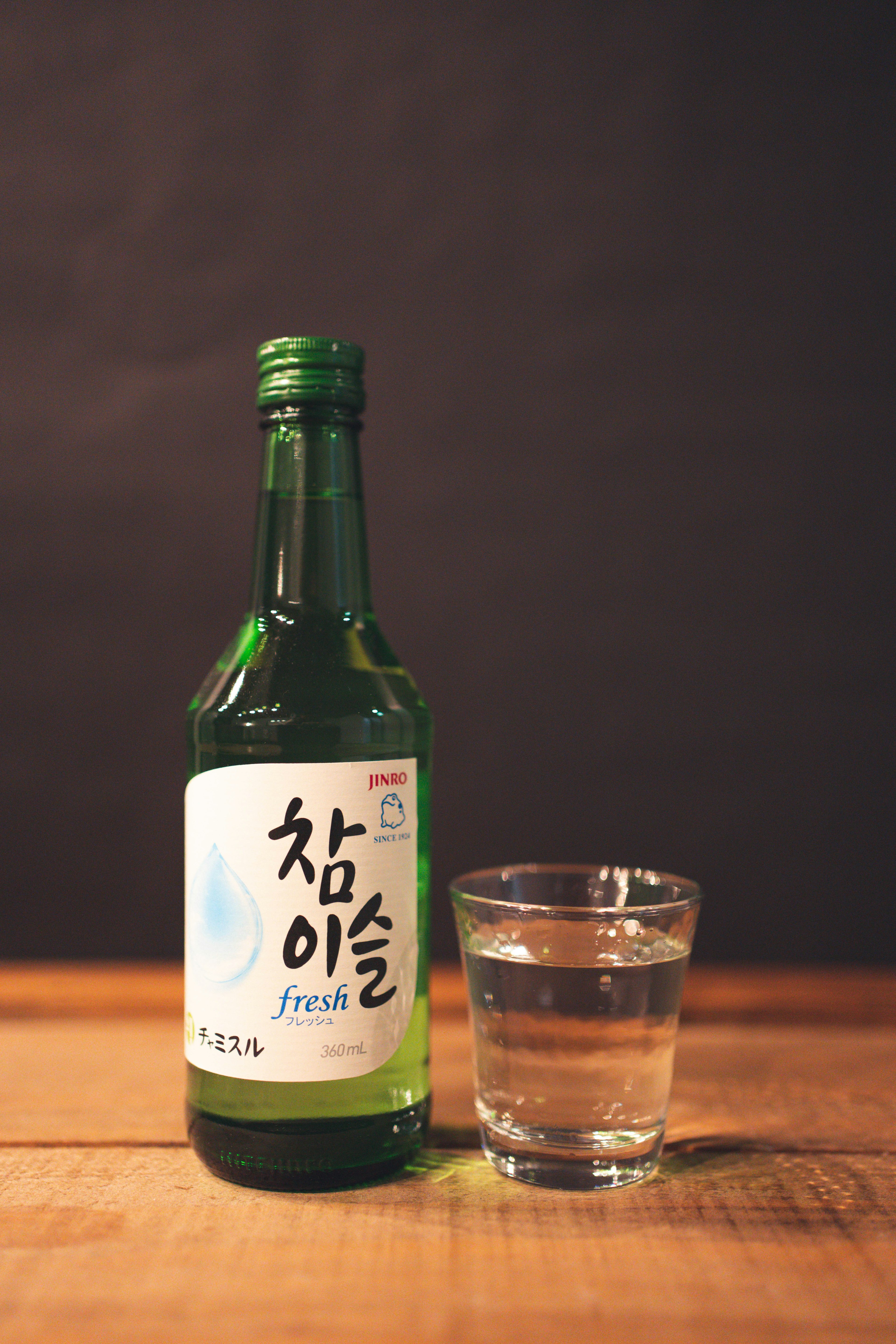 A green bottle of Korean soju next to a clear glass on a wooden table