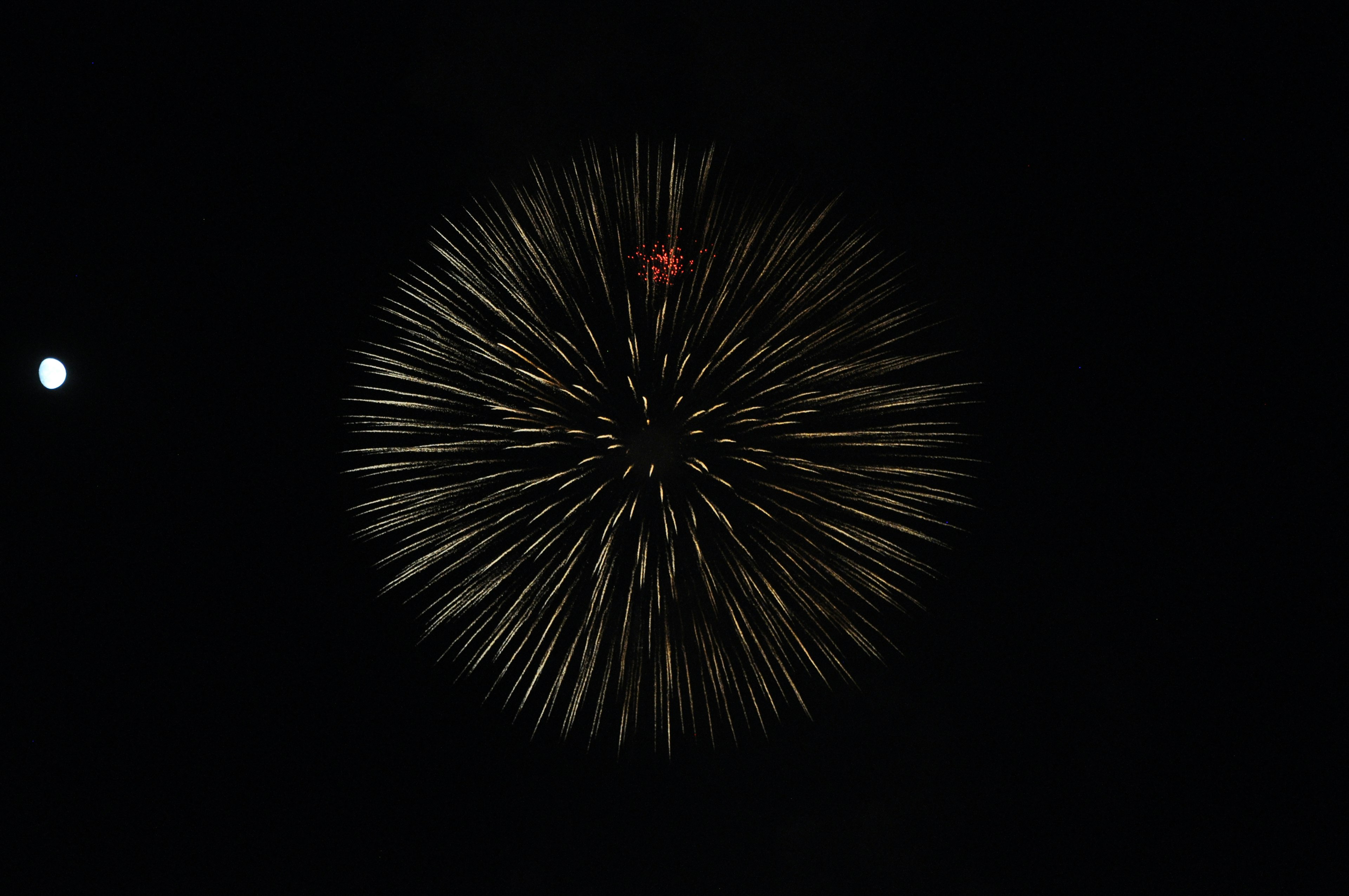 Explosion de feu d'artifice avec des couleurs vives sur un fond noir et une petite lune