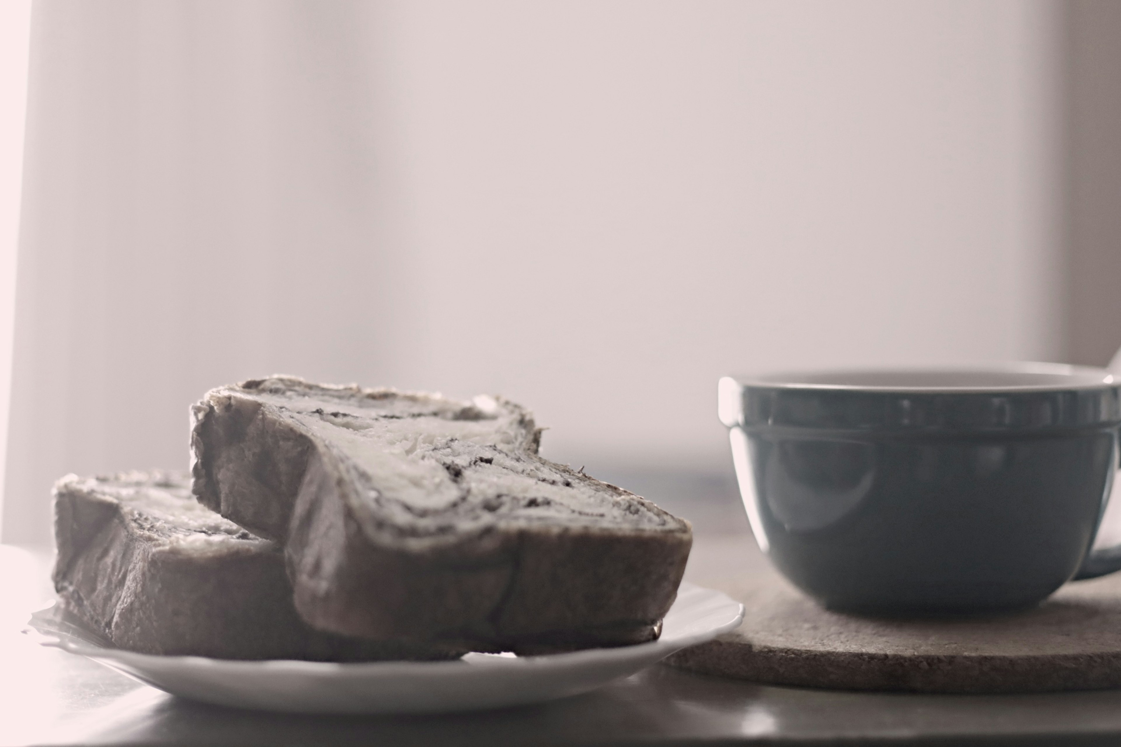 Iris roti di piring di samping cangkir kopi biru