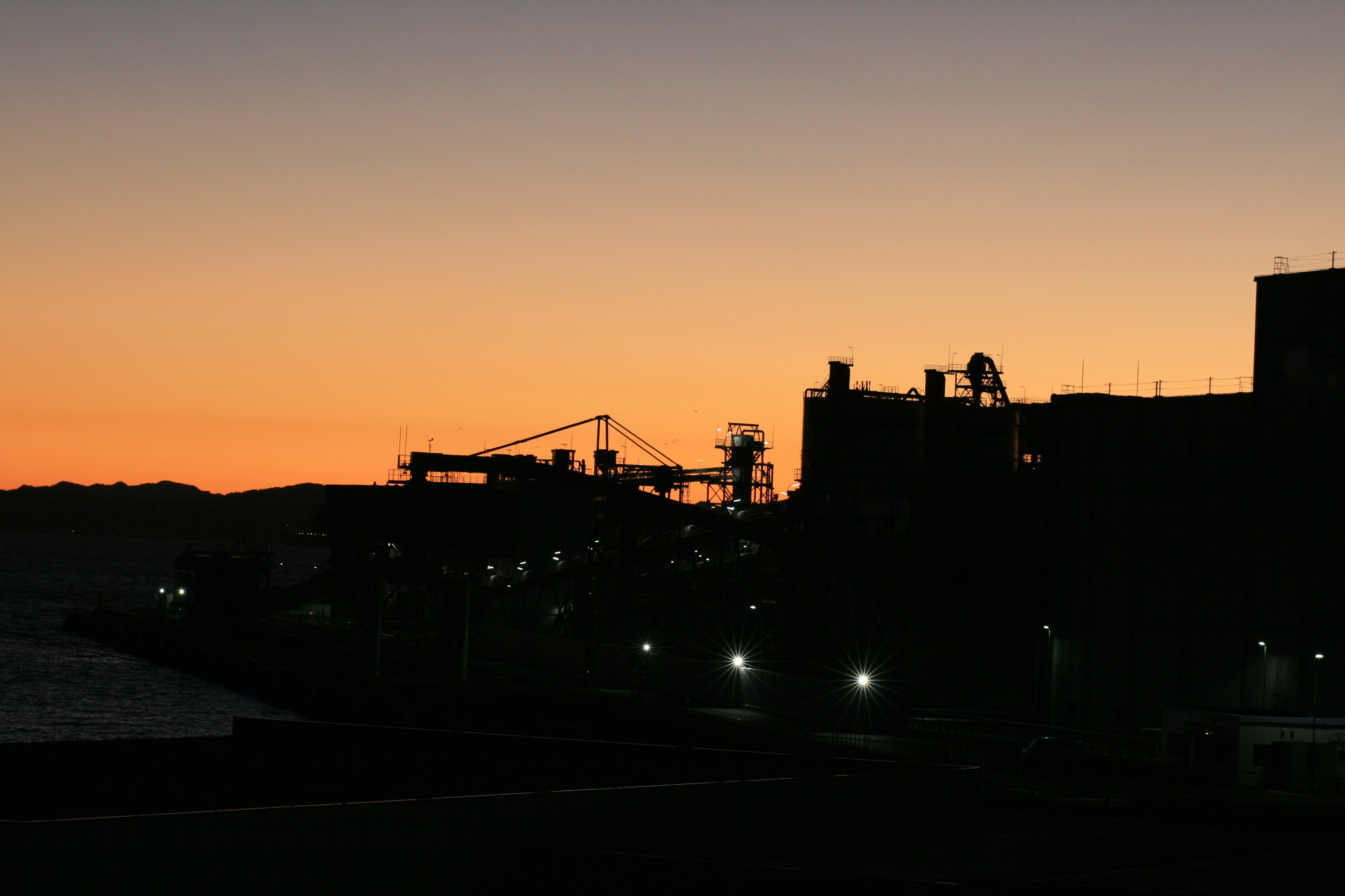 Silhouette of factories against a sunset sky