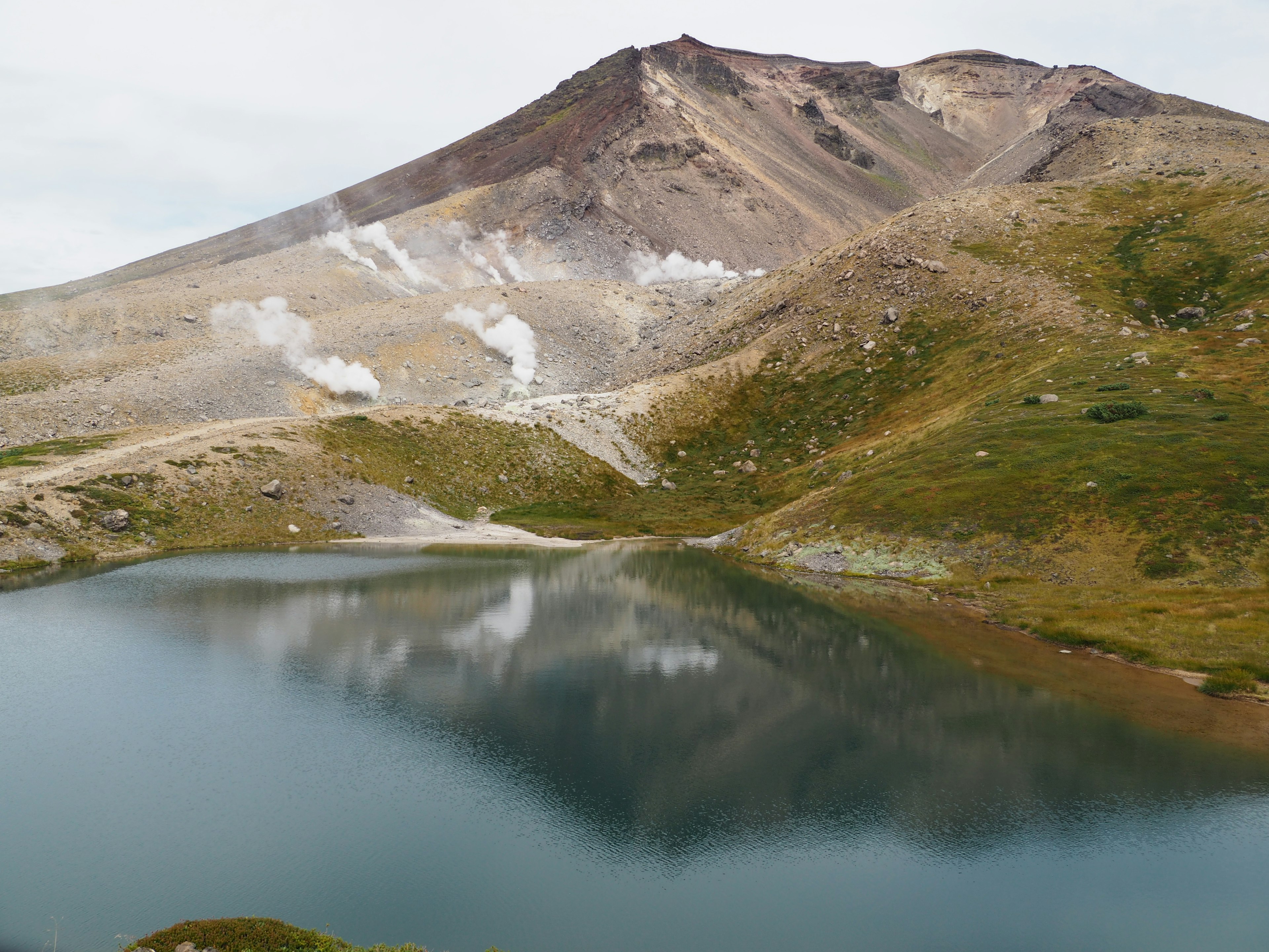 ทะเลสาบที่สวยงามสะท้อนภูเขาพร้อมไอน้ำที่ลอยขึ้นจากเนินเขา