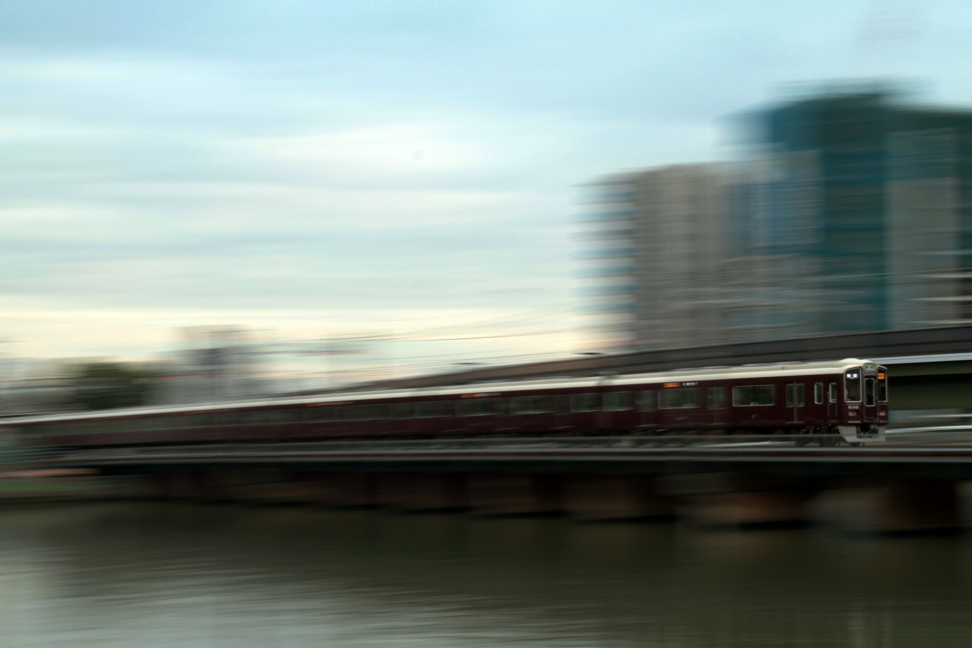 A blurred train in motion alongside modern buildings near a body of water