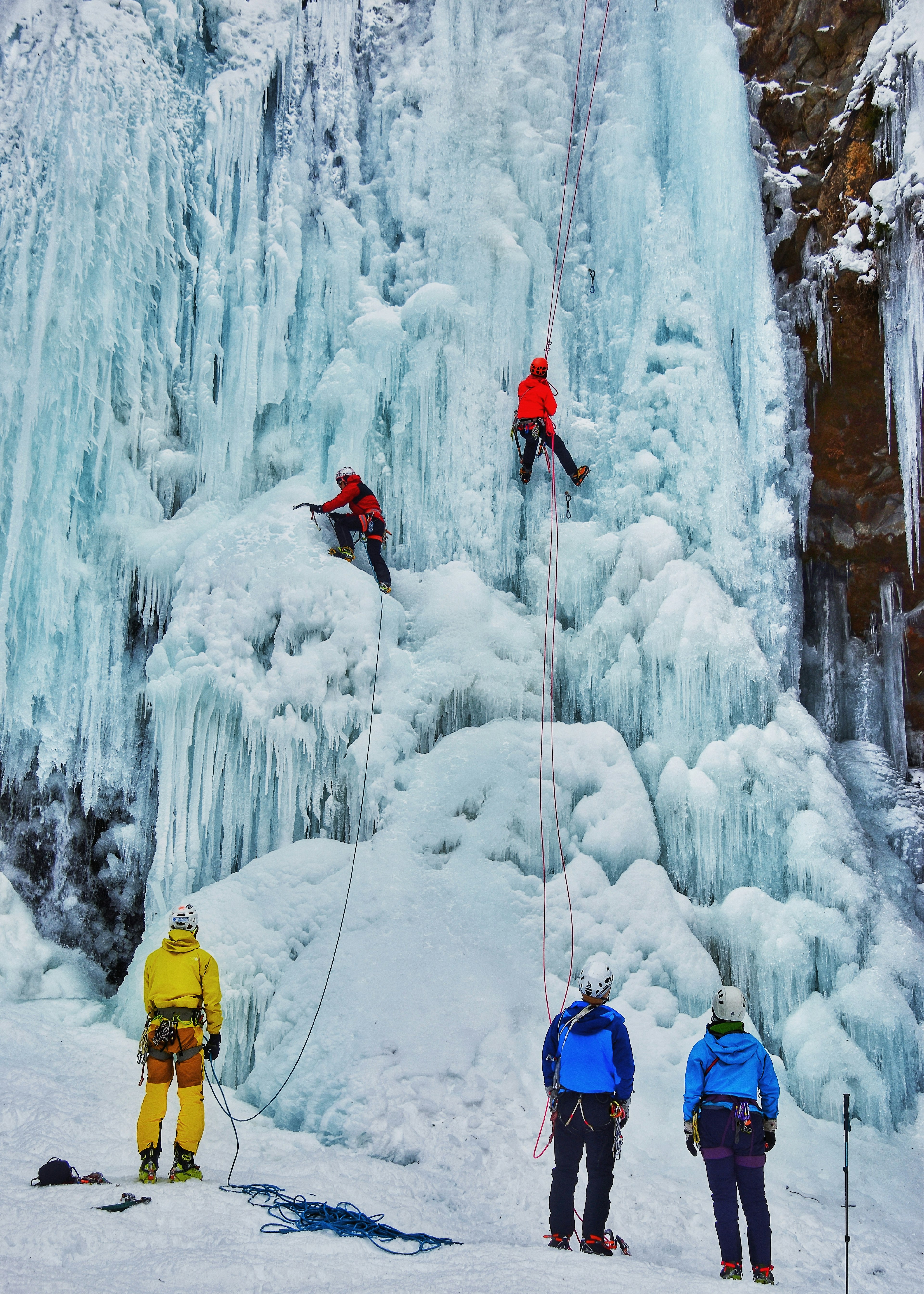 Escaladores ascendiendo una cascada de hielo con observadores abajo