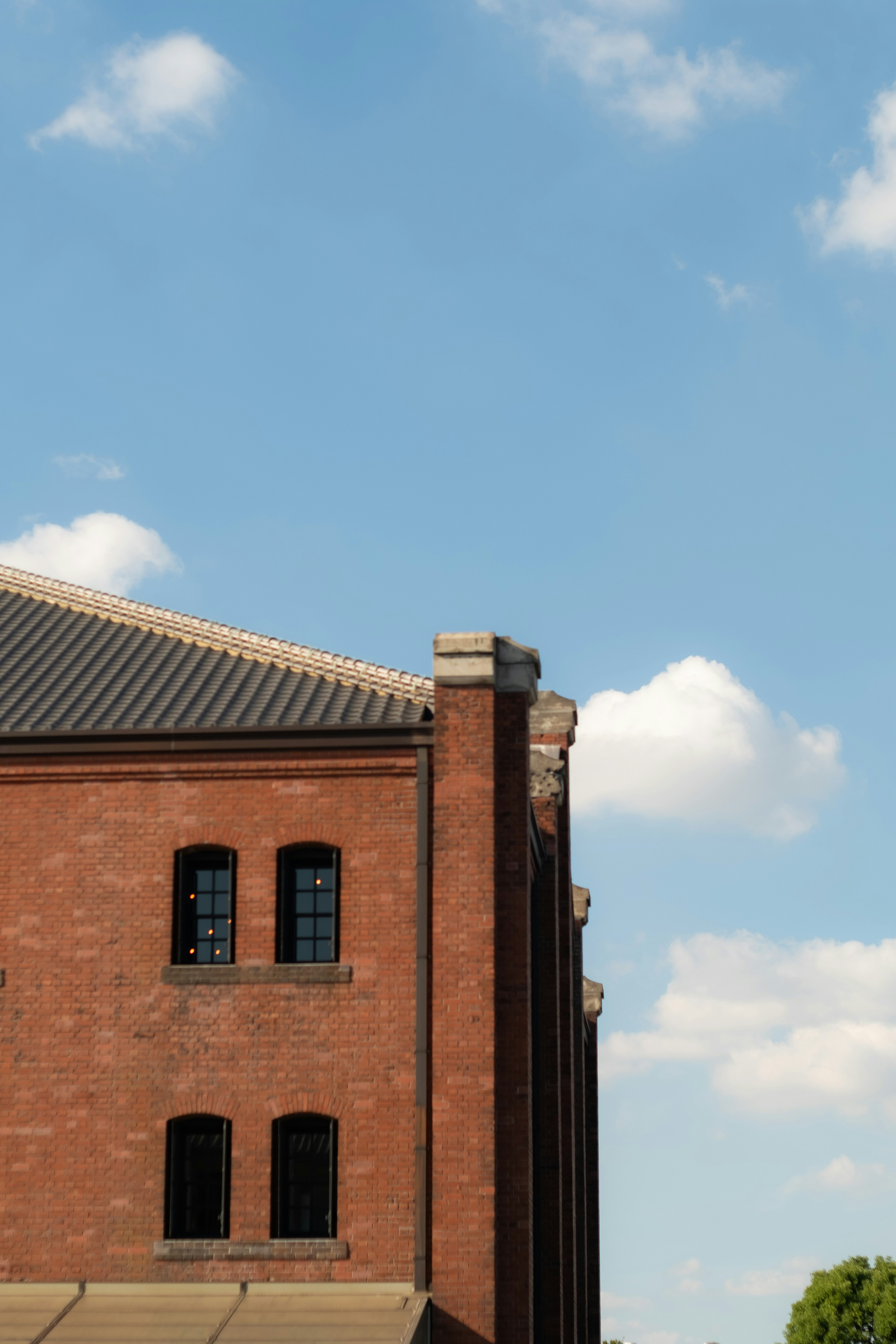 Part of a red brick building under a blue sky featuring windows and roof design