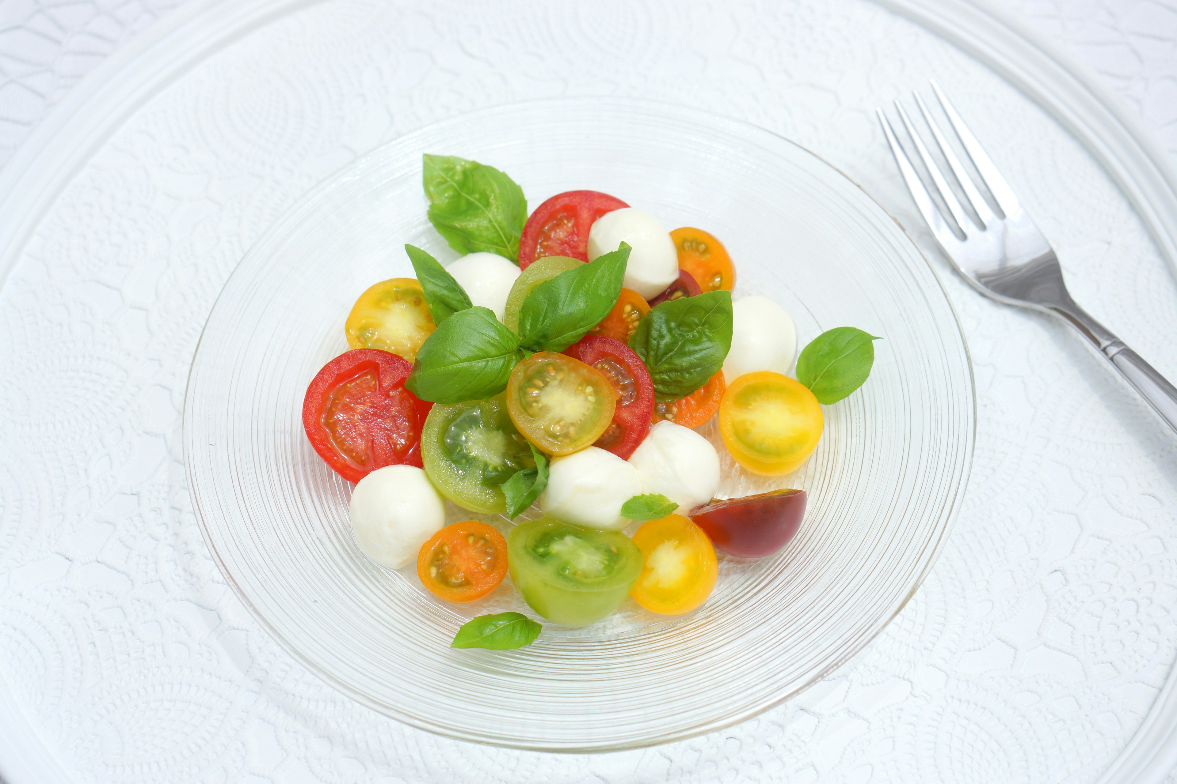 Una ensalada colorida con varios tomates y bolitas de mozzarella decorada con hojas de albahaca fresca