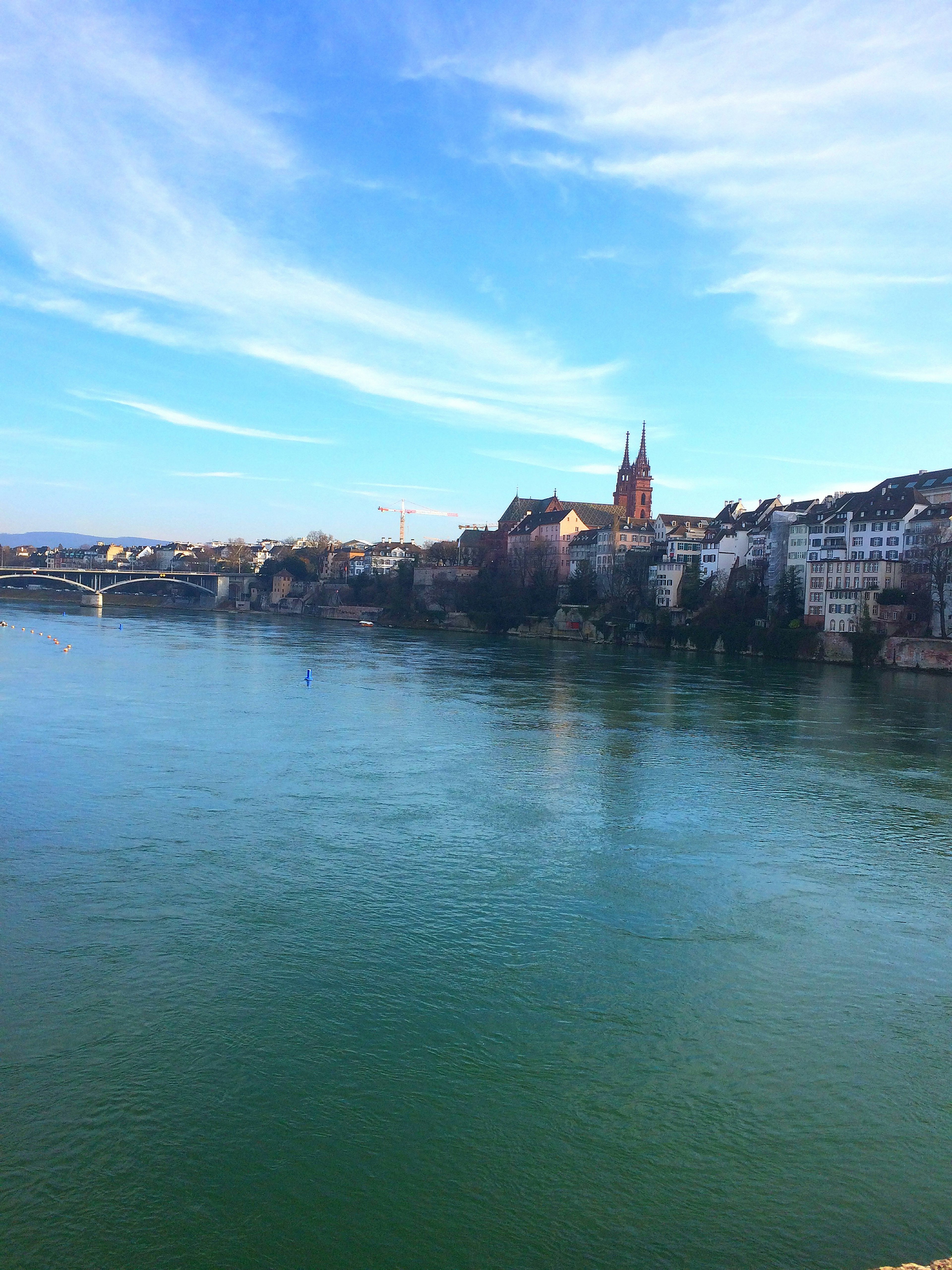 Vista panoramica di un fiume con acqua verde e cielo blu che mostra lo skyline di Basilea e le torri delle chiese