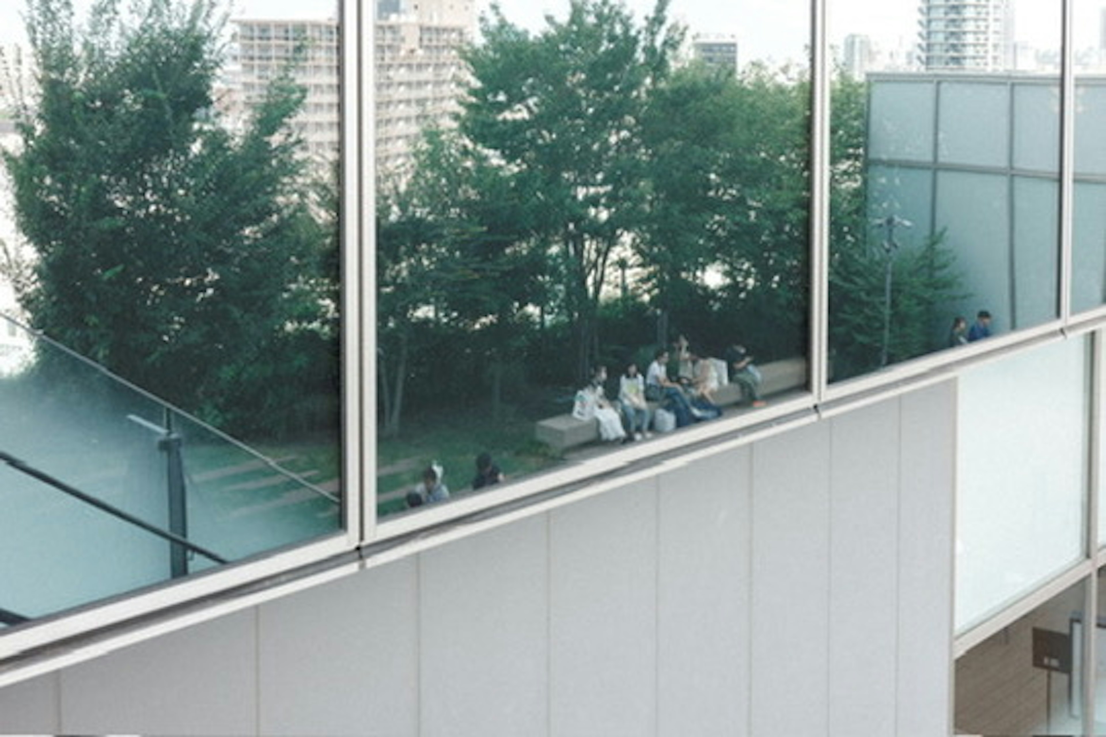 Des personnes assises dans un parc urbain reflétées dans des fenêtres en verre