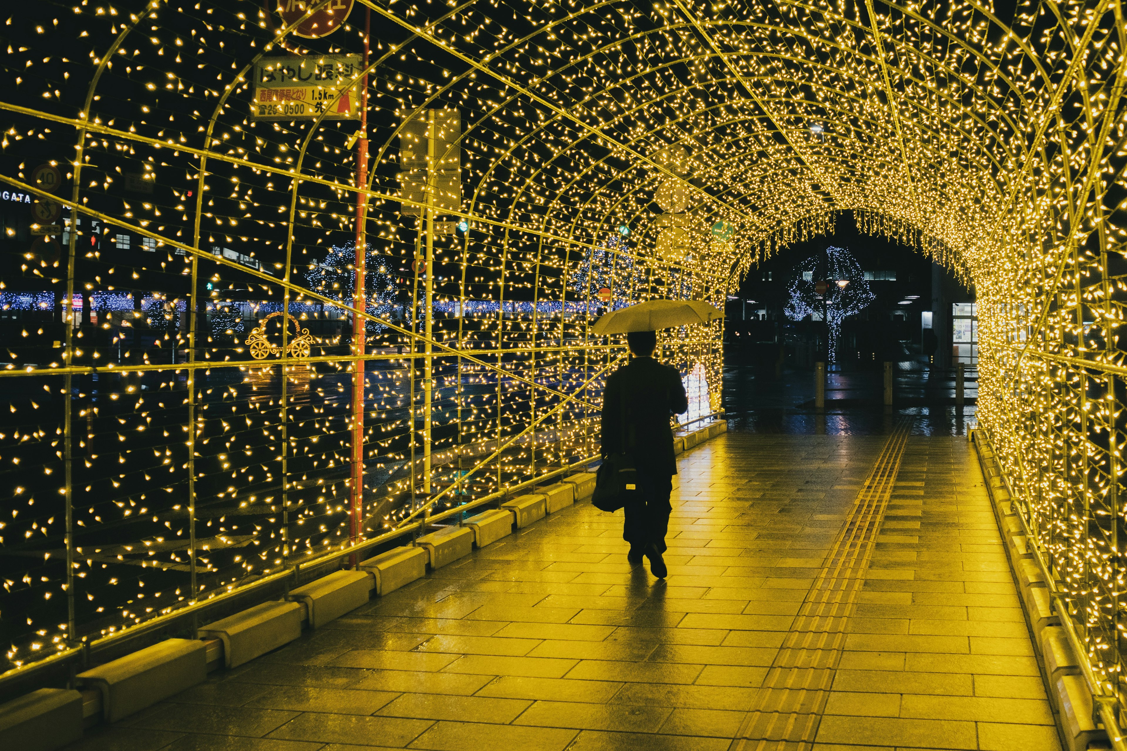 Person walking through a tunnel of lights with an umbrella