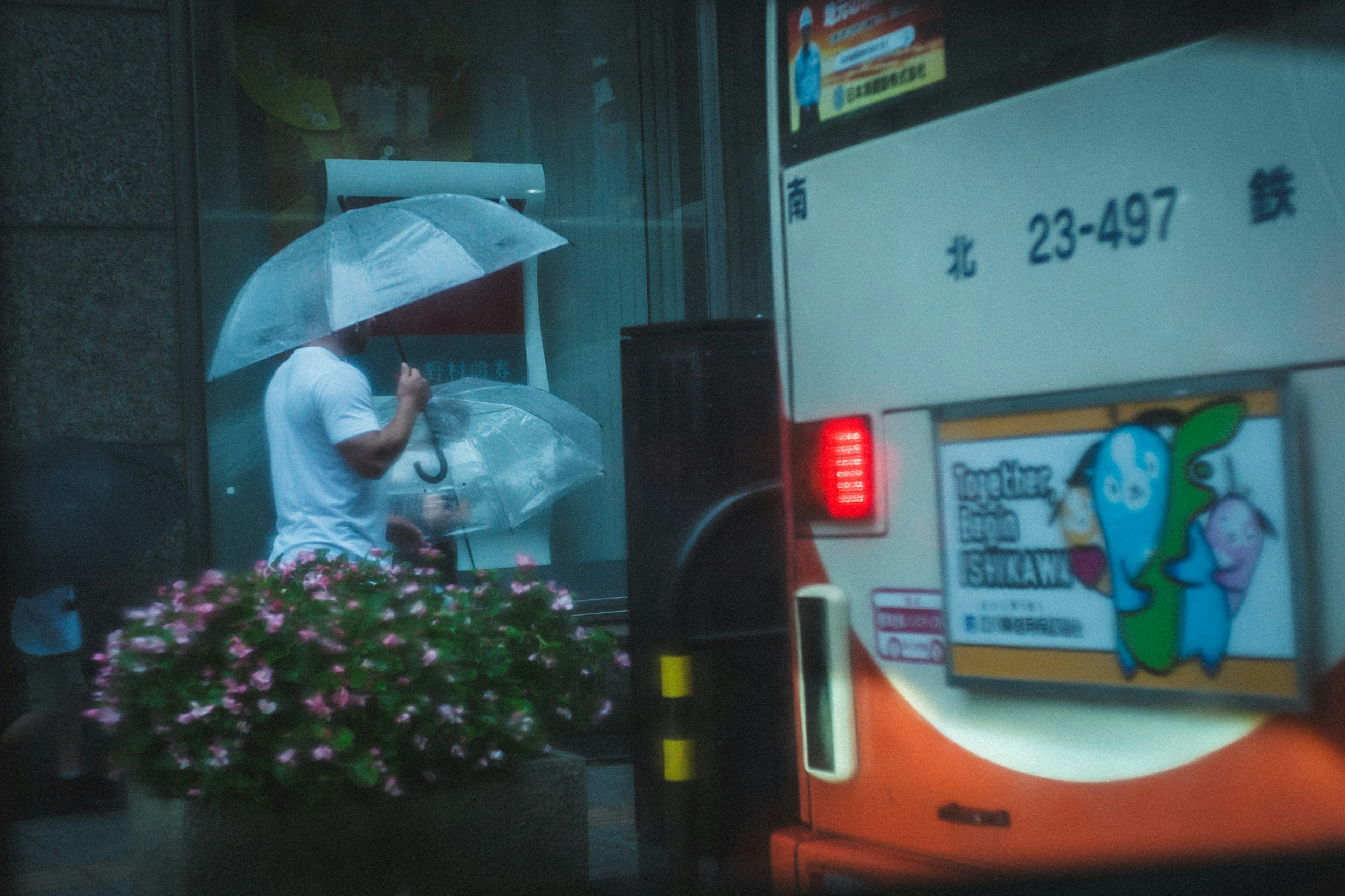 白い傘を持った男性が花の前に立っているバス停の風景