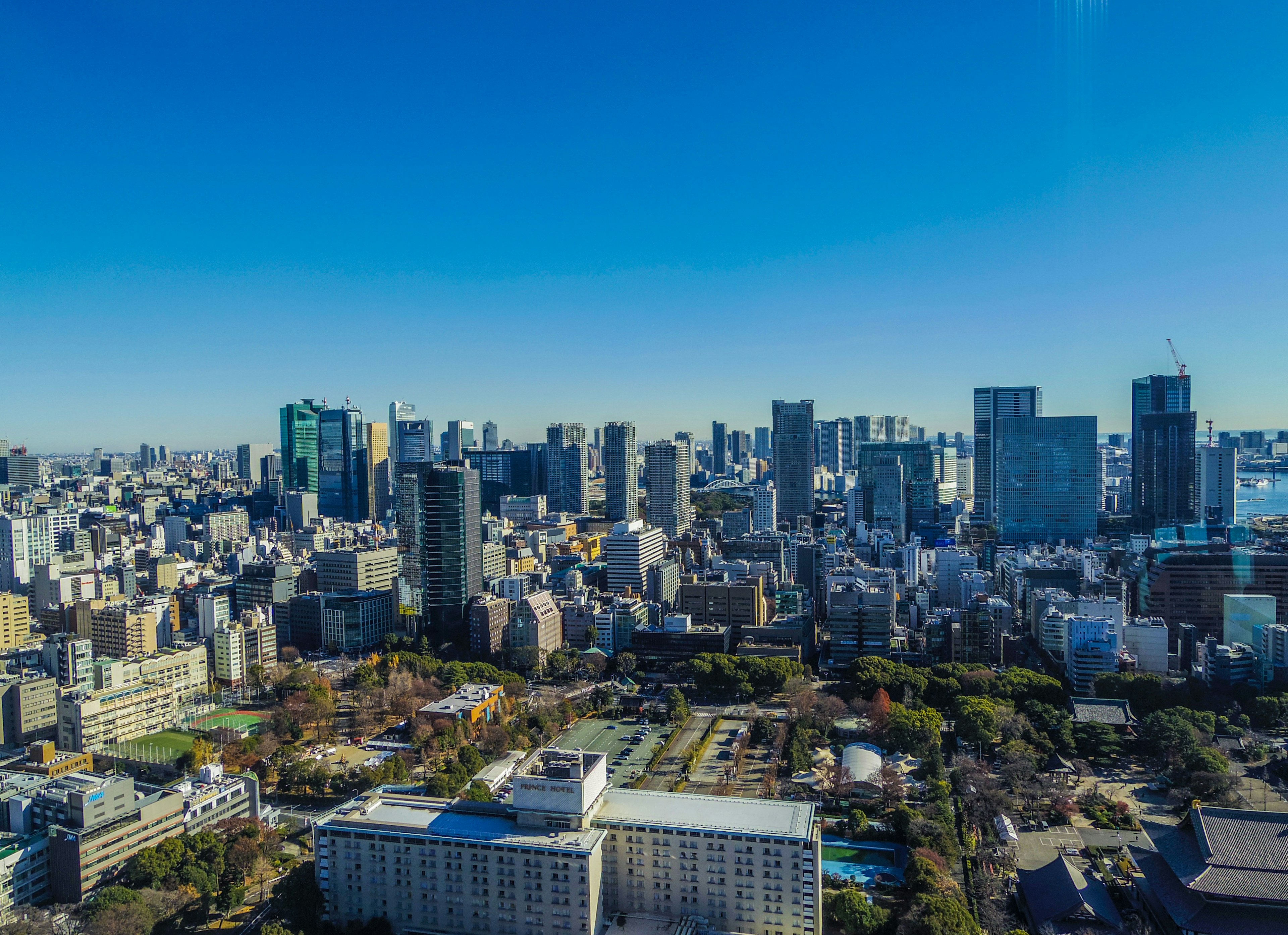 Pemandangan udara dari cakrawala Tokyo menampilkan gedung pencakar langit dan taman hijau di bawah langit biru yang cerah