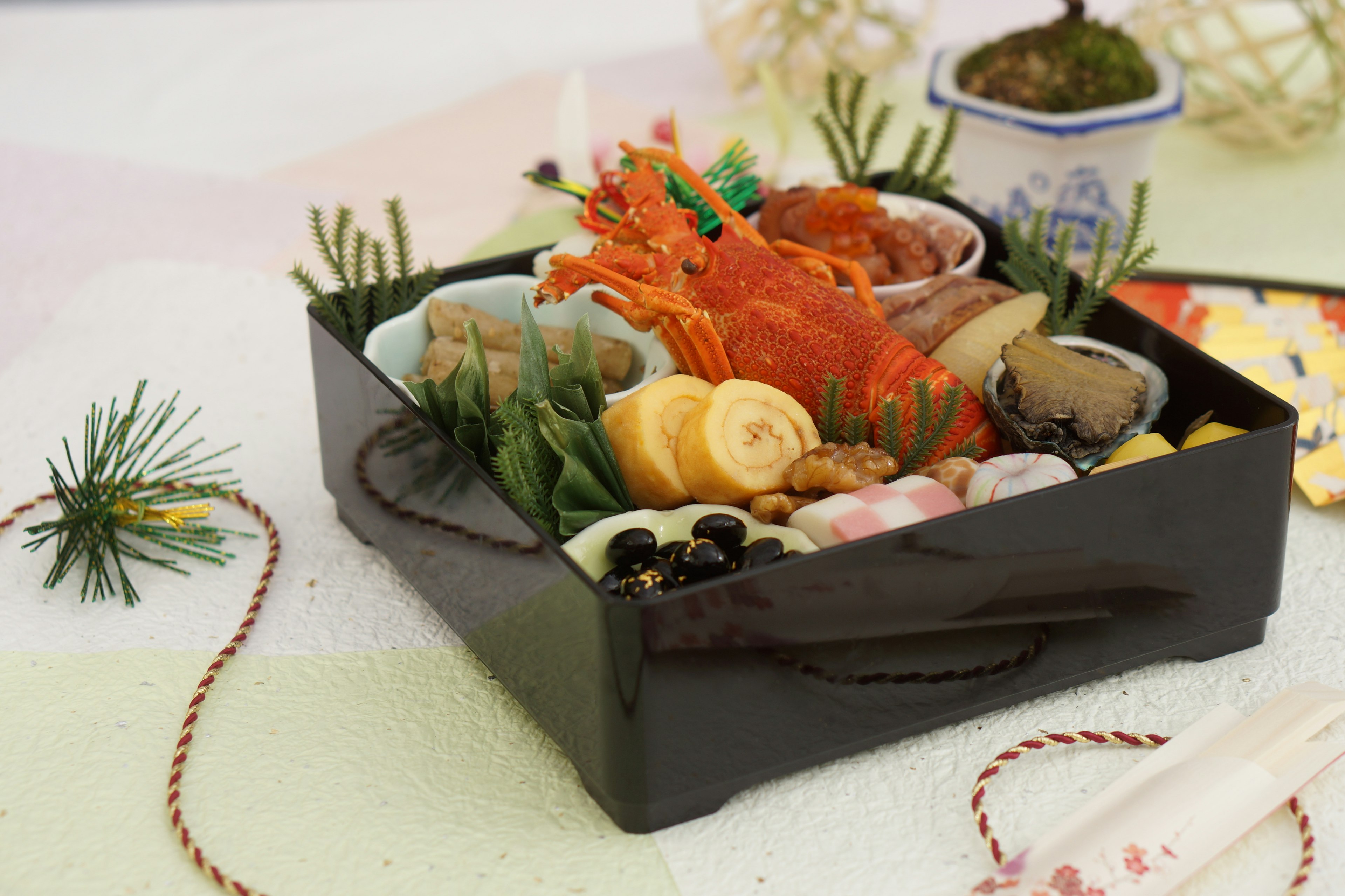 A black lacquered box filled with colorful osechi cuisine featuring salmon shrimp vegetables and mochi