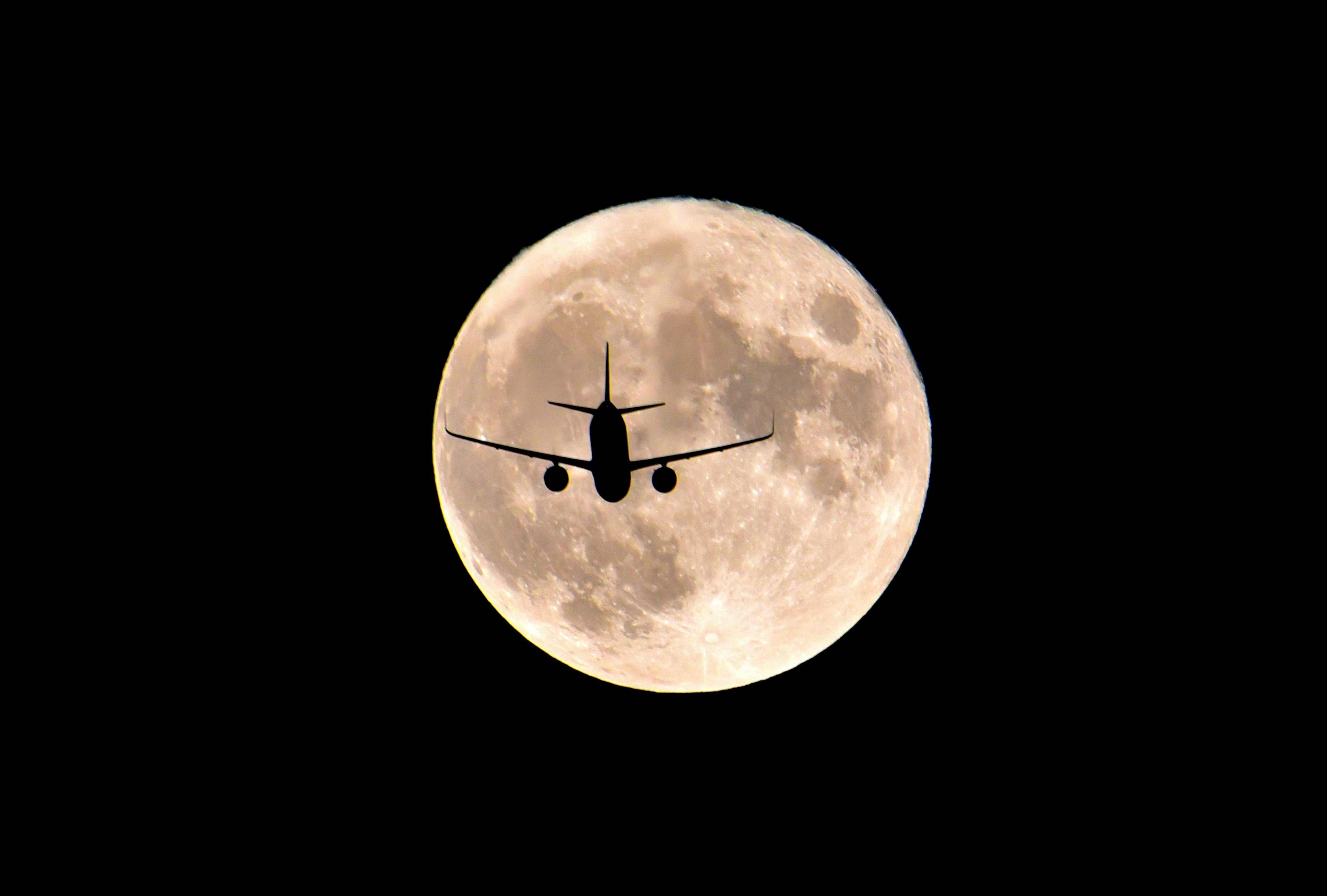 Silhouette of an airplane flying in front of the moon