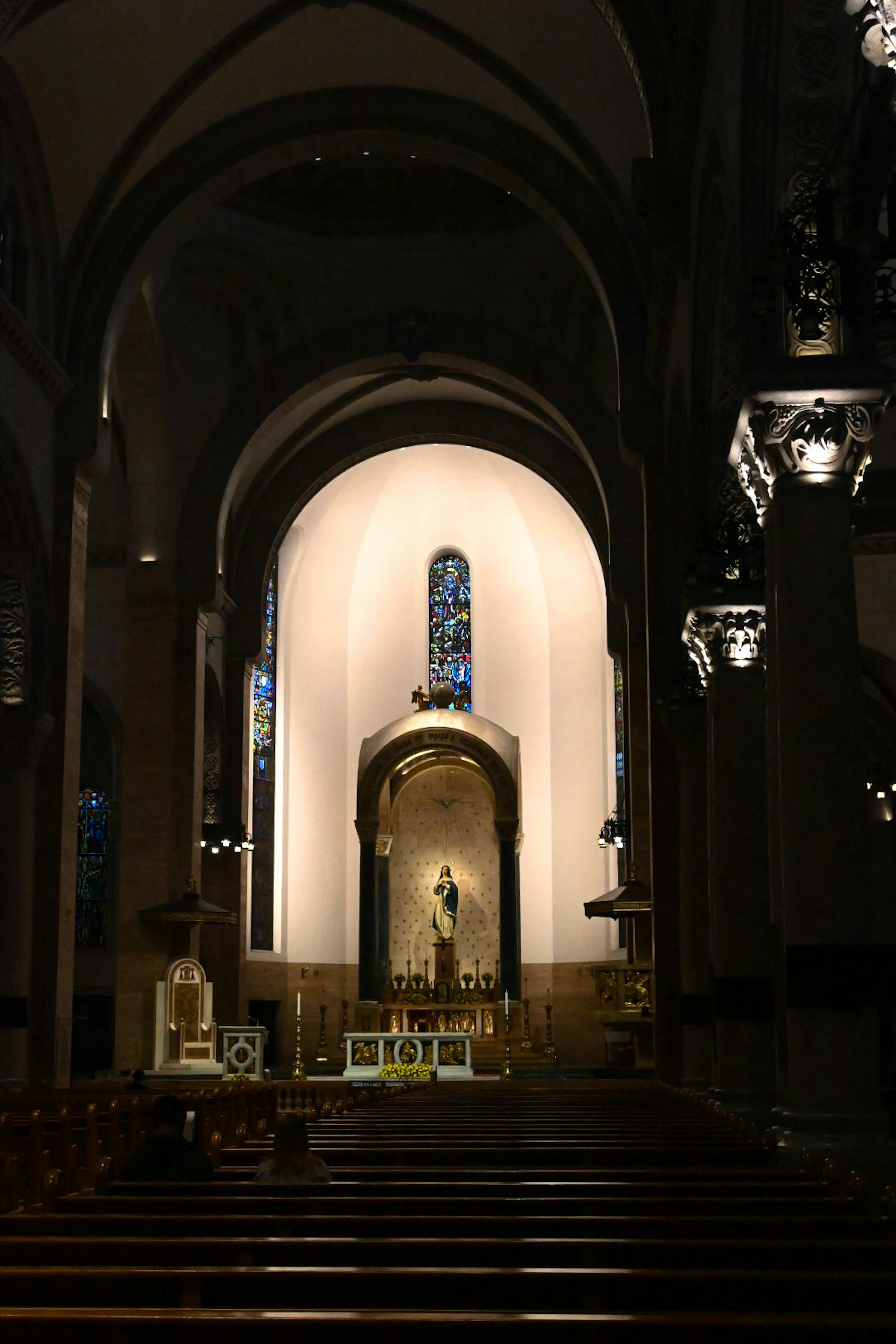 Interior of a cathedral featuring a bright altar and stained glass windows