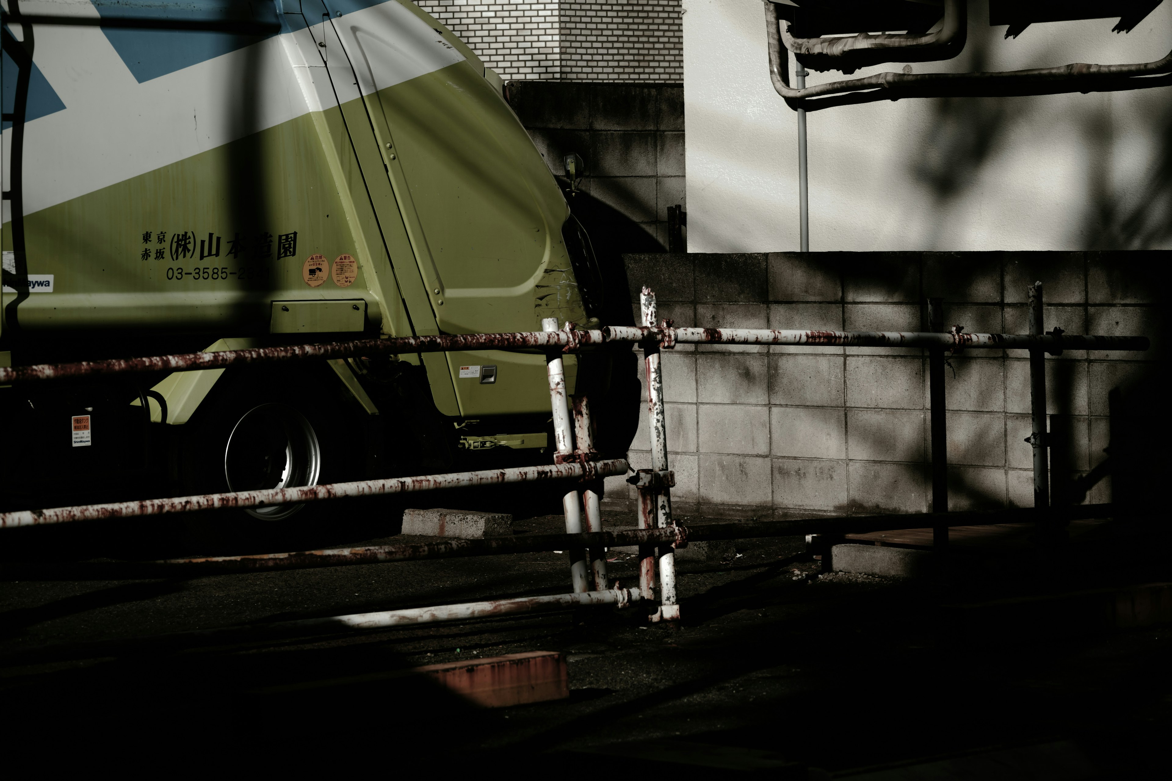 Urban scene featuring a green truck and shadowed wall