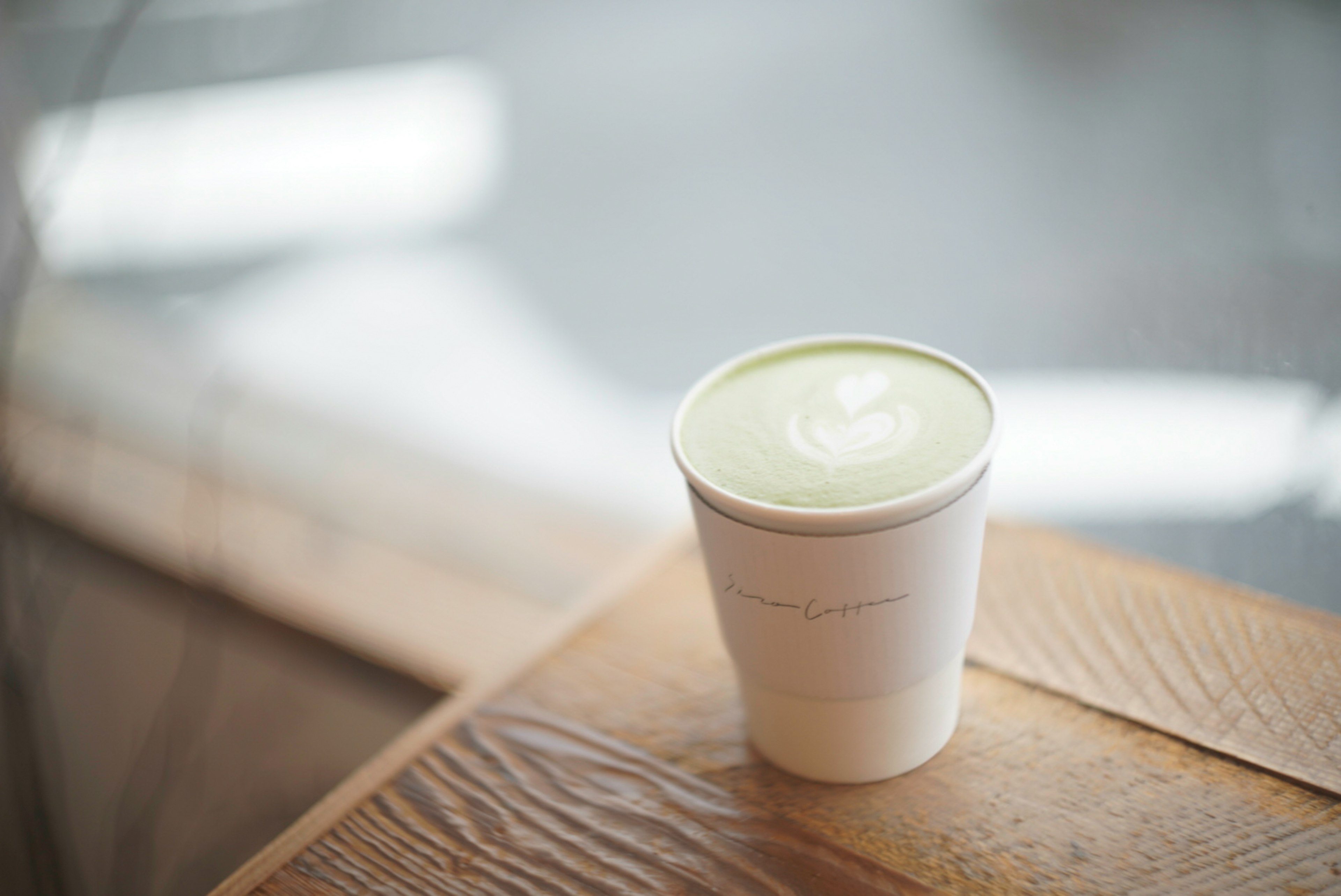 Una tazza bianca con latte di tè verde posata su un tavolo di legno