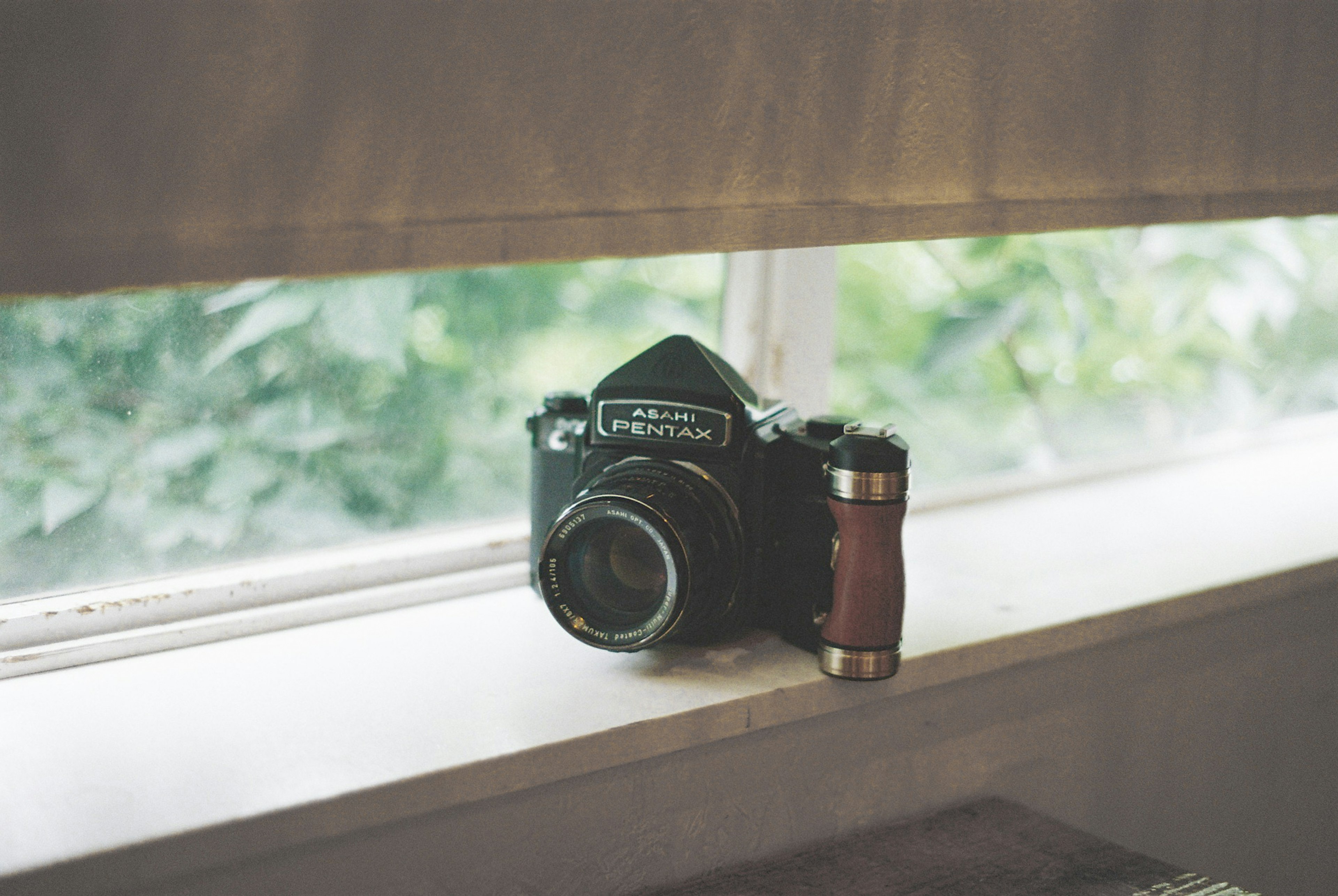 Film camera resting on a windowsill with a green background