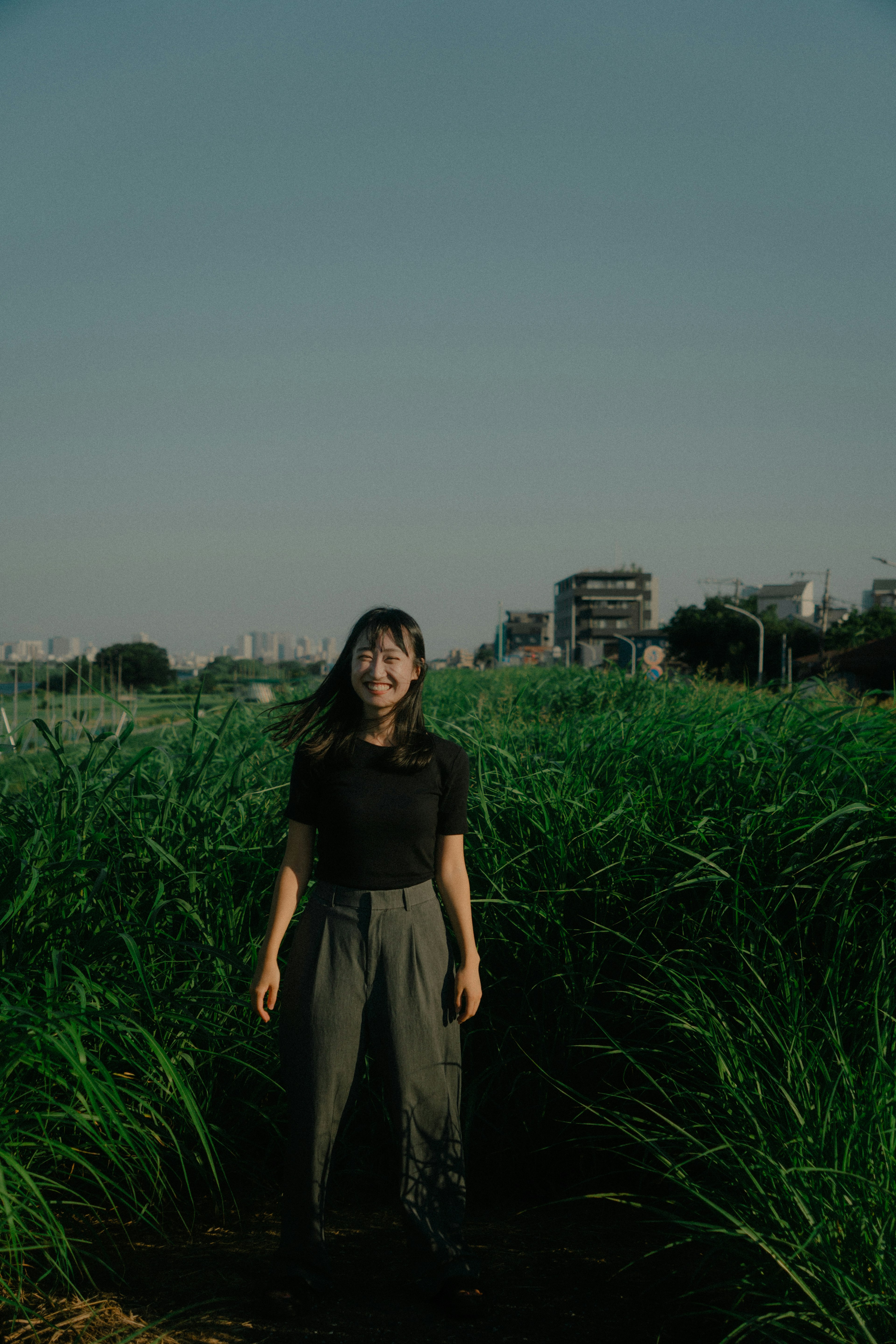 一名女性站在高草中，背景是城市風景