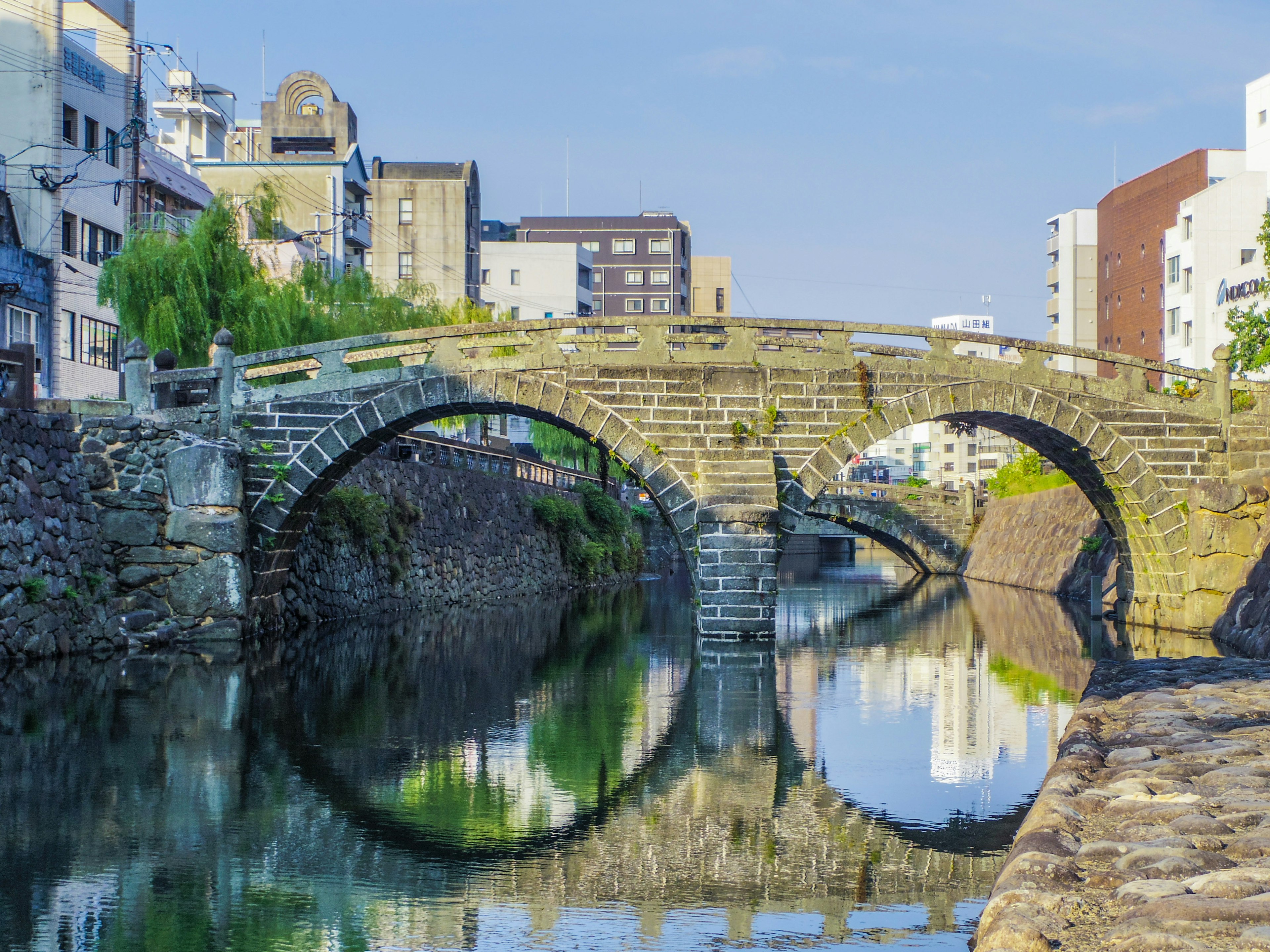 Steinbogenbrücke, die sich im ruhigen Wasser mit Gebäuden im Hintergrund spiegelt