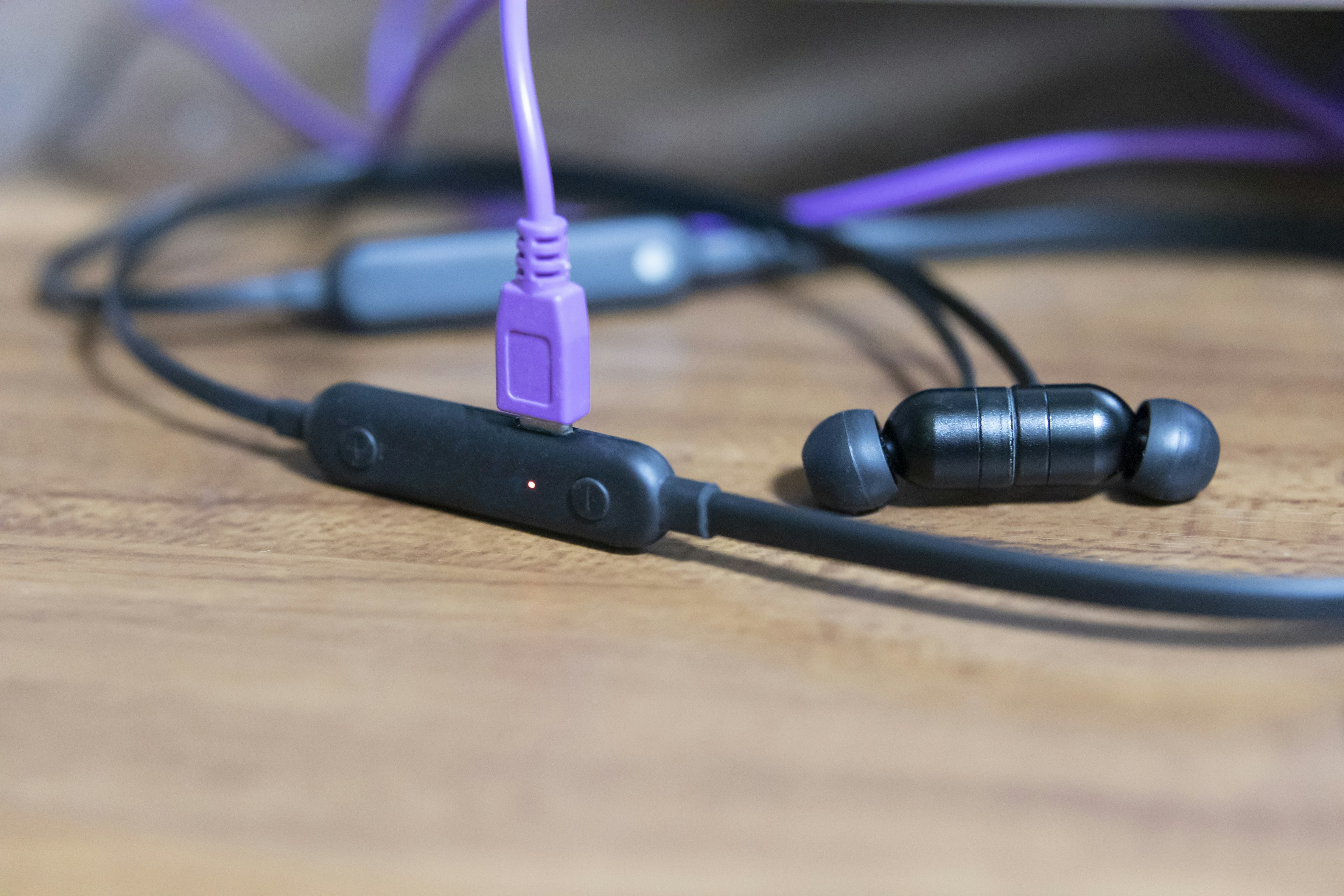 Black earbuds with a controller connected by a purple cable