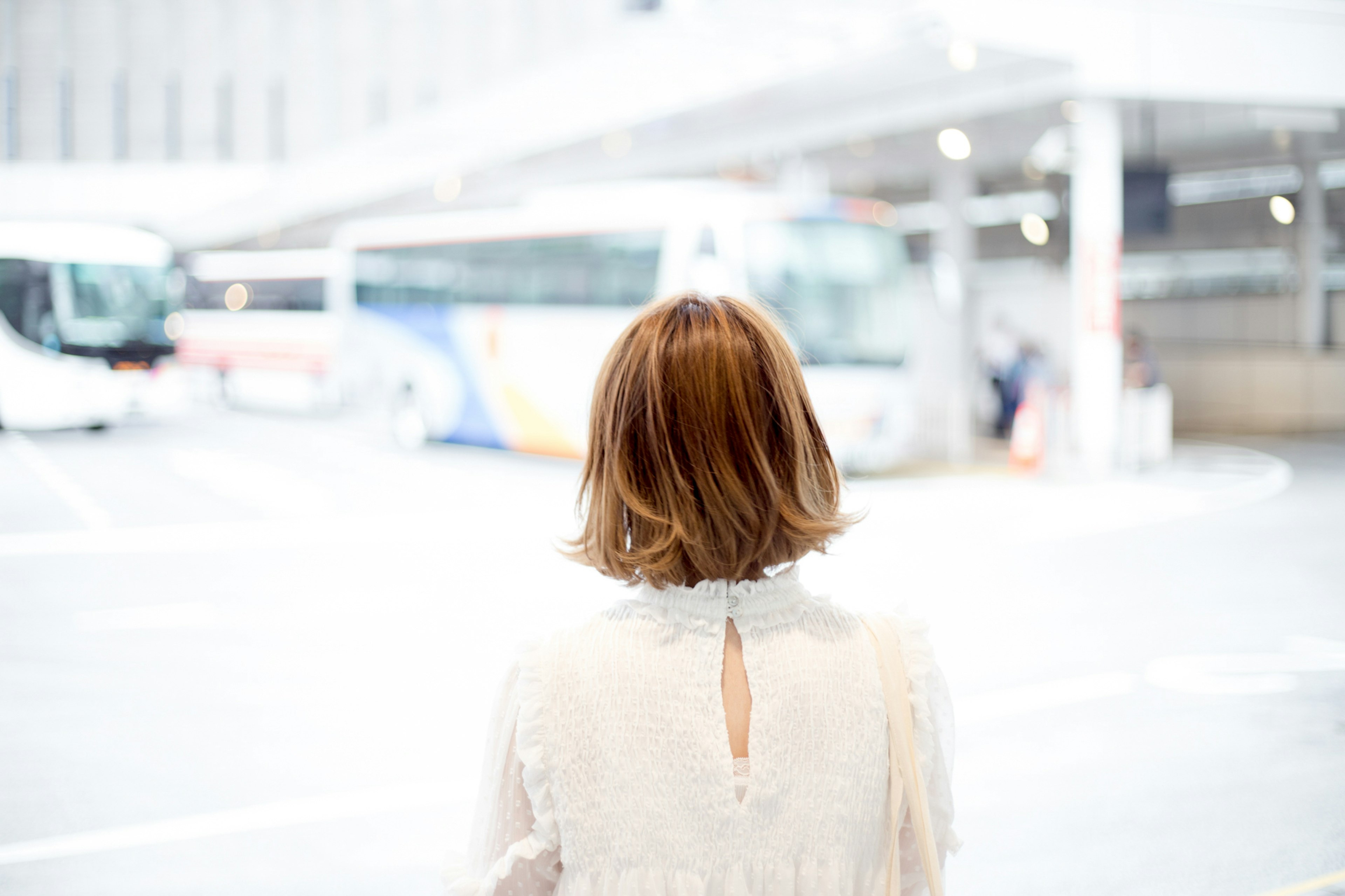 Una mujer esperando en una parada de autobús con autobuses al fondo