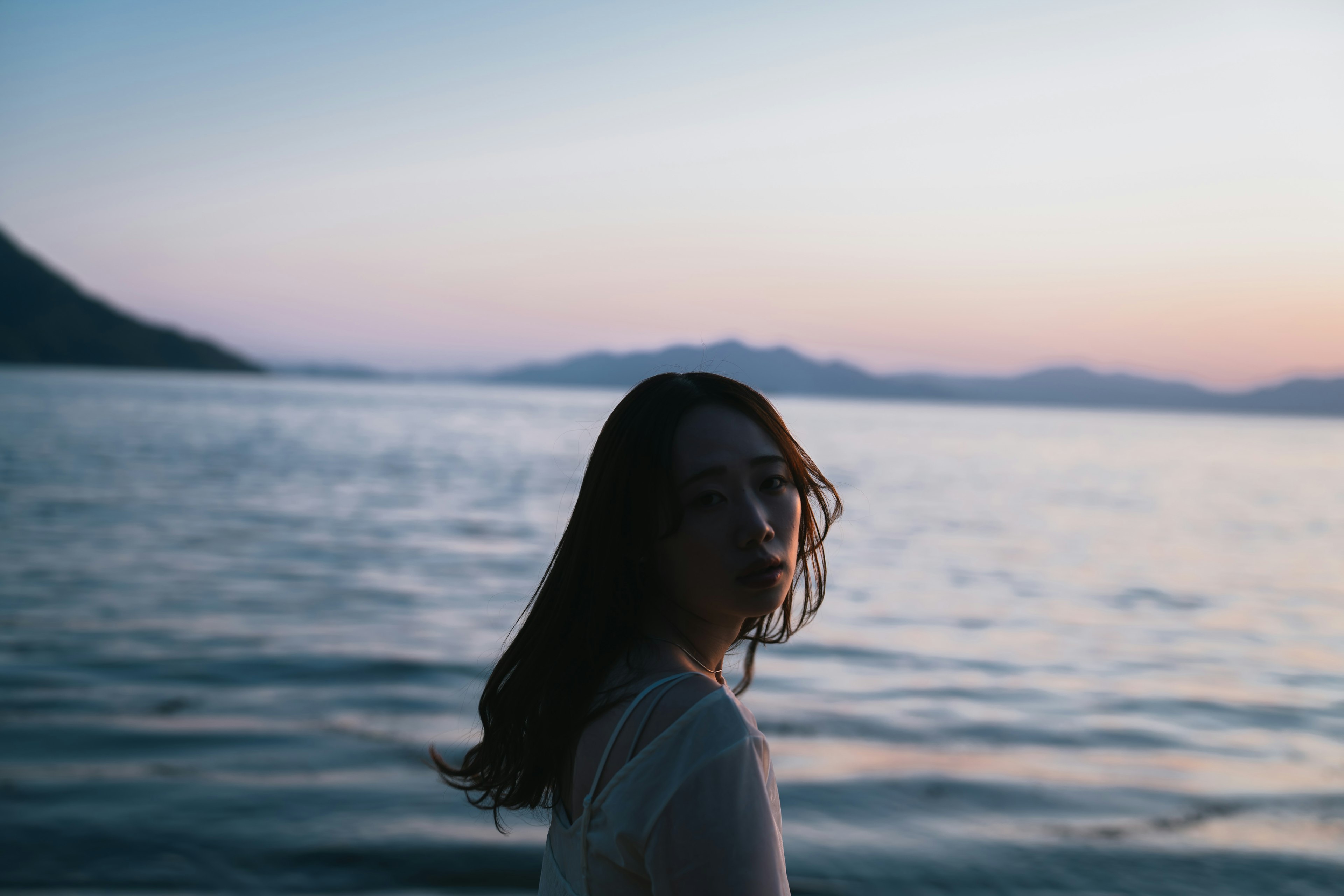 海辺で振り返る女性のシルエットと夕焼けの背景