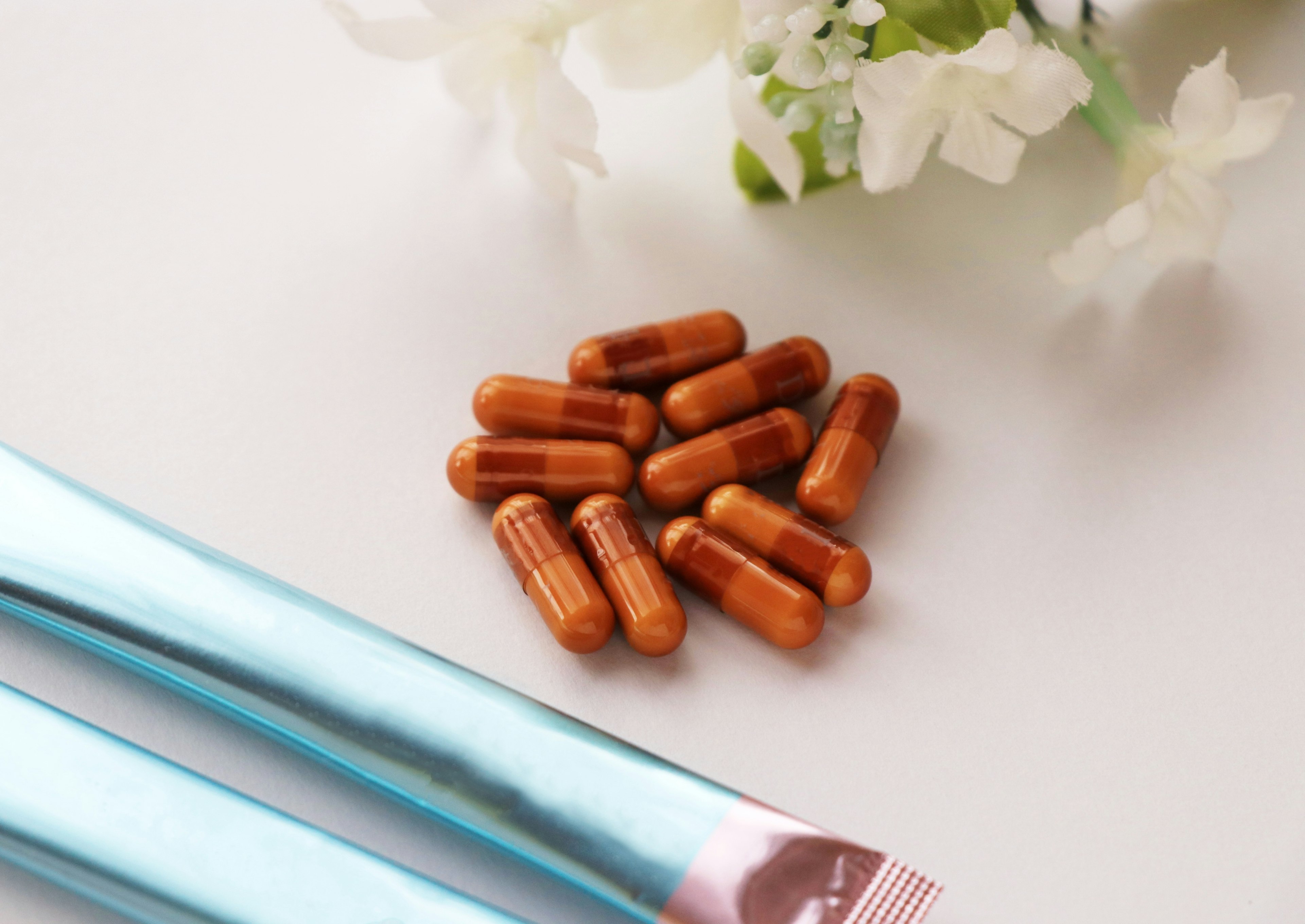 A simple composition featuring orange capsules and a blue packaging alongside white flowers