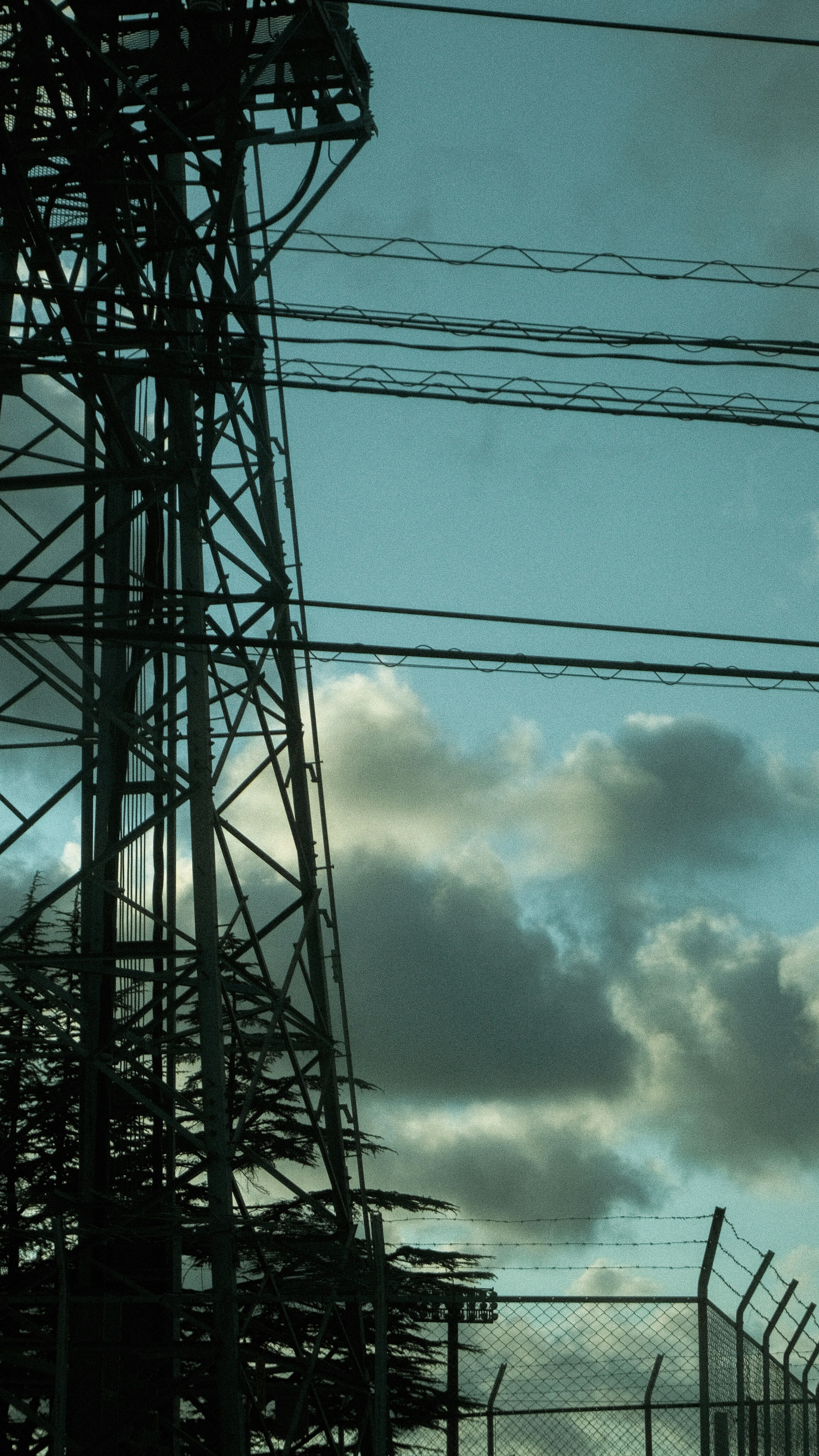 Silhouette of a power tower and power lines against a blue sky with clouds