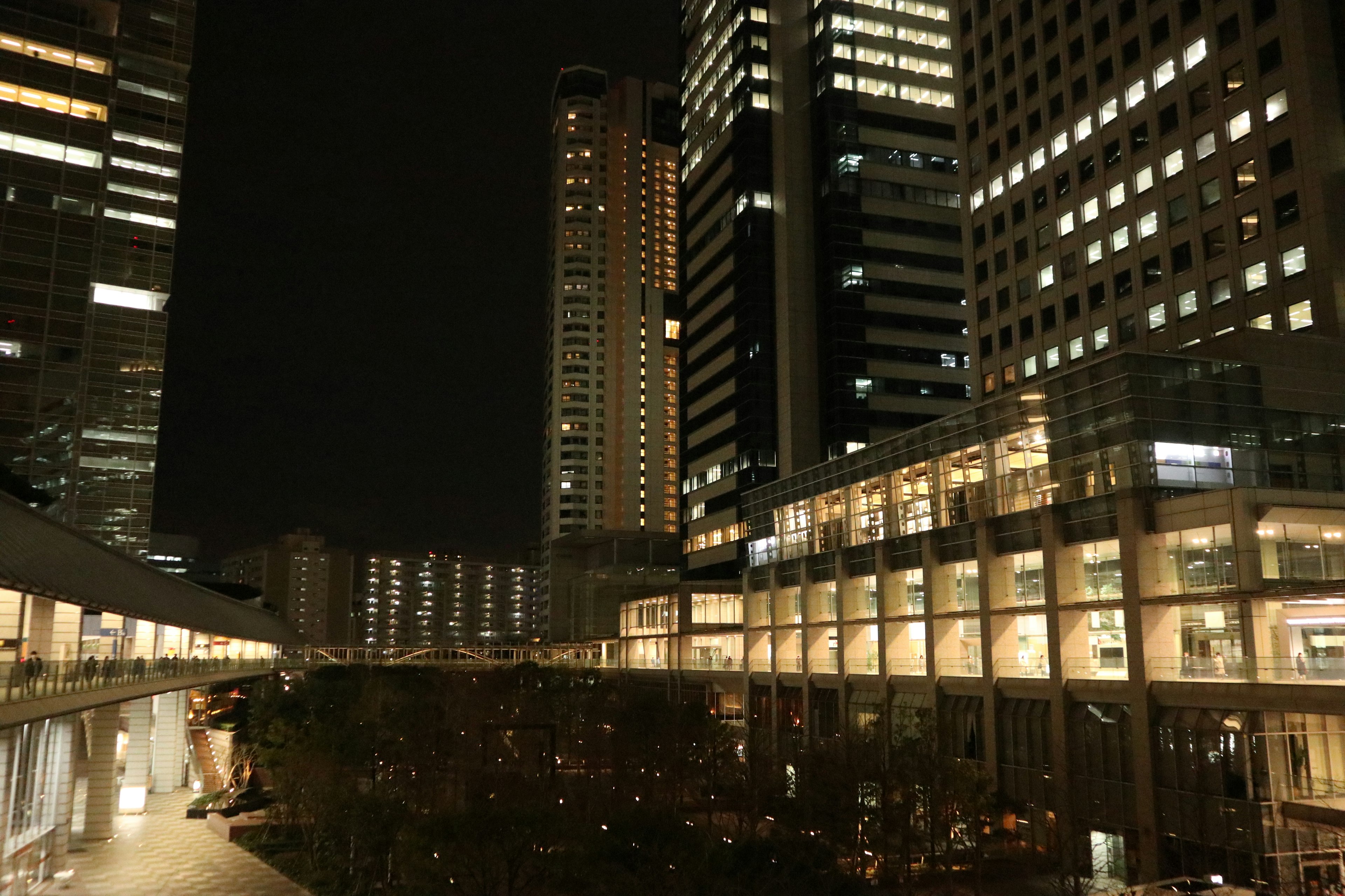 Paisaje urbano nocturno con rascacielos y luces brillantes junto a áreas verdes y arquitectura moderna