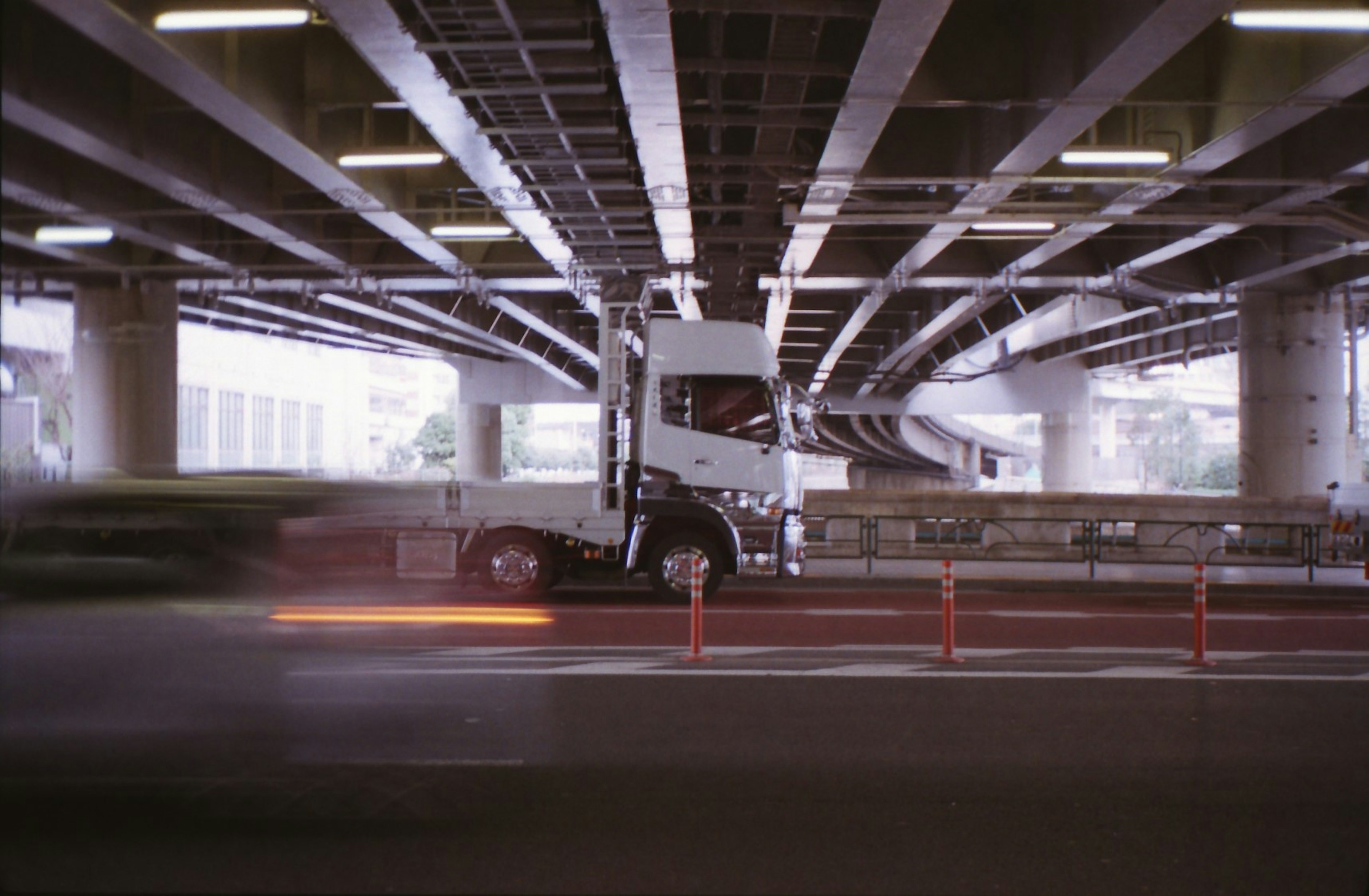 Truck parked under an overpass with moving vehicles in the foreground