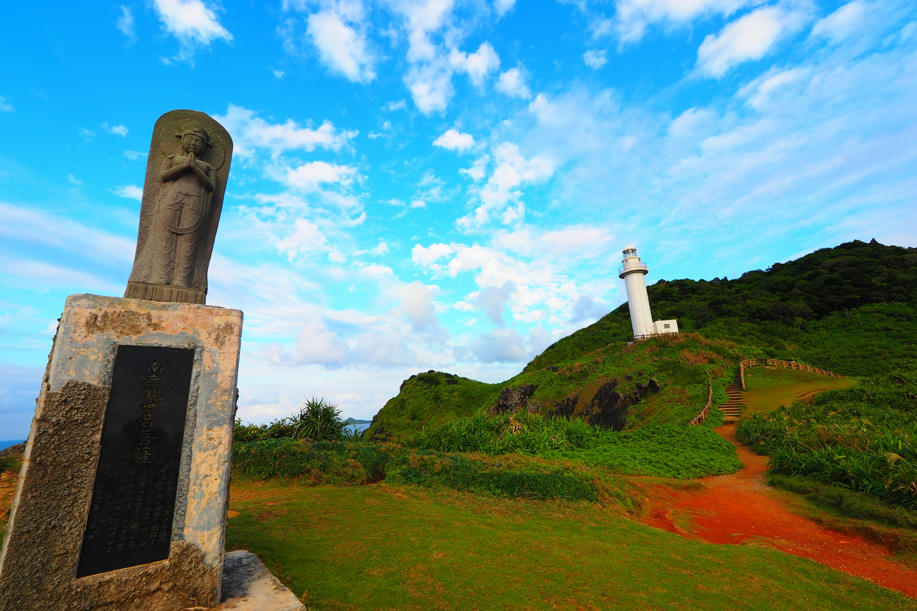 Paysage avec un phare et un monument sur une colline sous un ciel bleu et de l'herbe verte