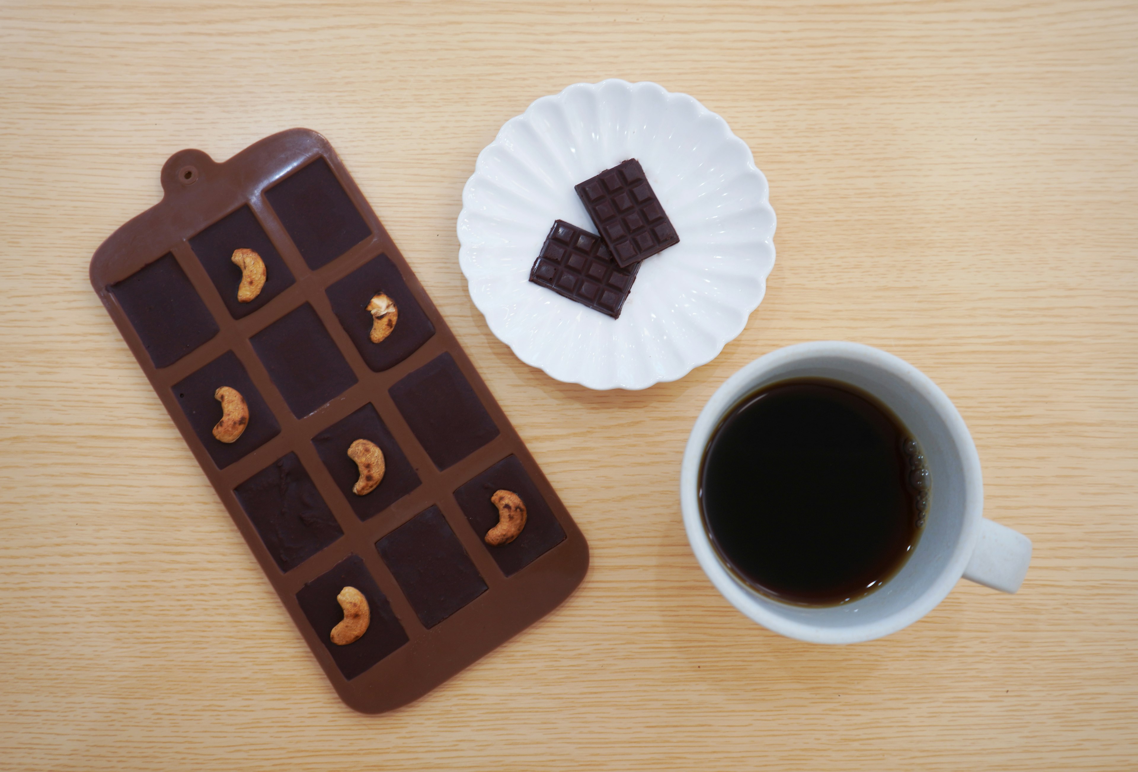 Gambar cokelat dengan kacang mete dan secangkir kopi di atas permukaan kayu