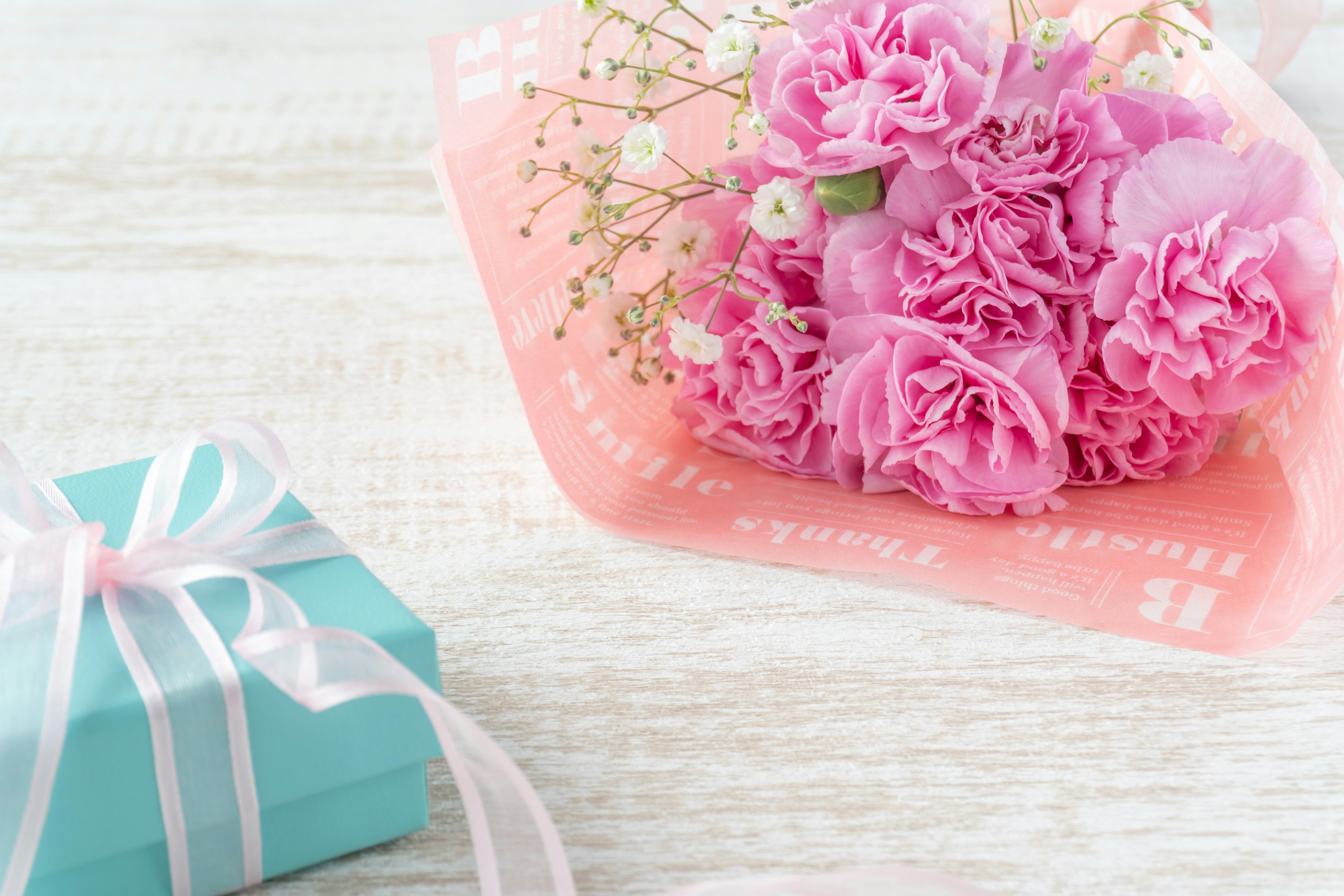 A bouquet of pink carnations and a blue gift box are placed together