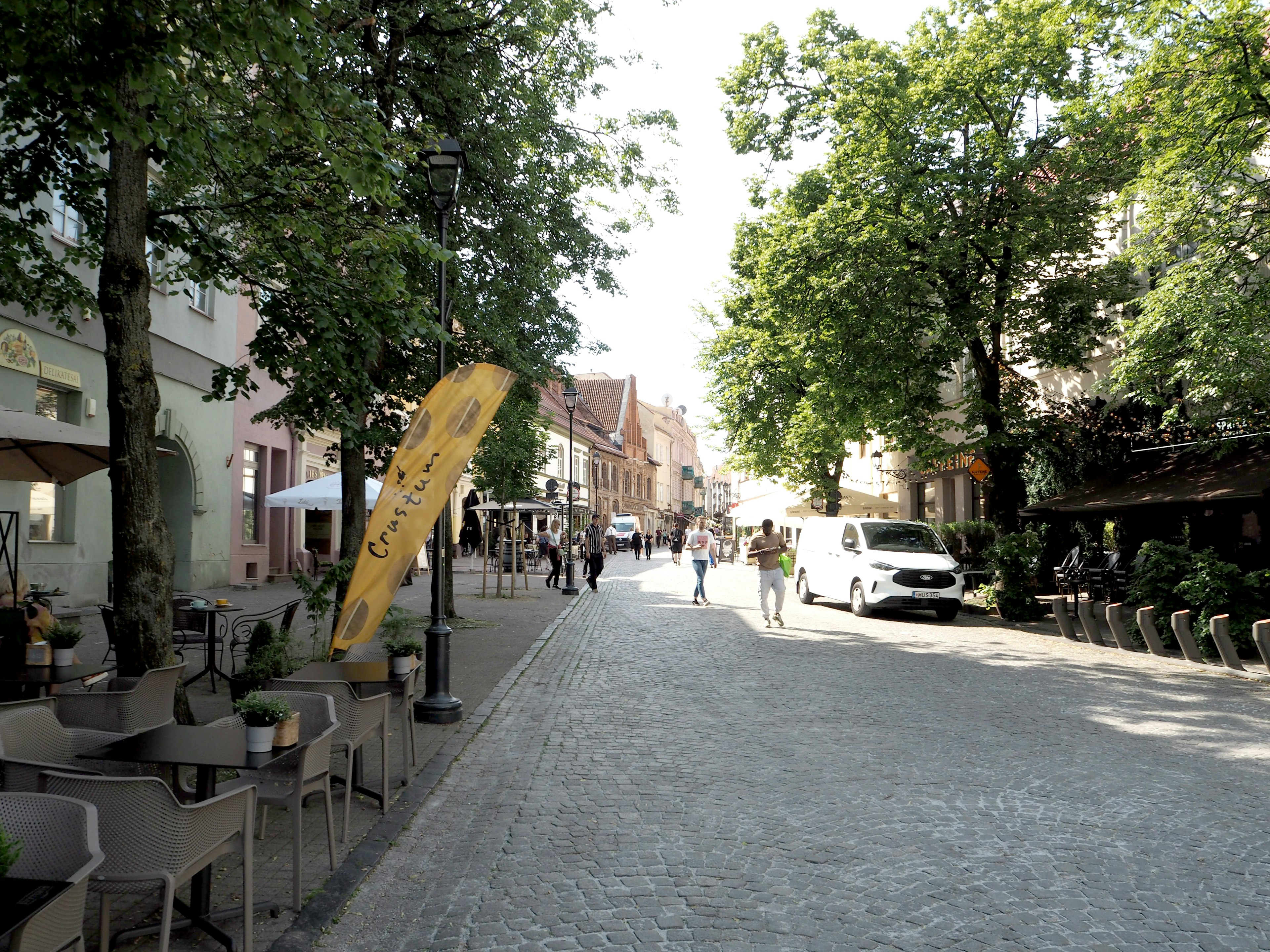 Une rue pavée bordée de cafés et de personnes entourée d'arbres verts