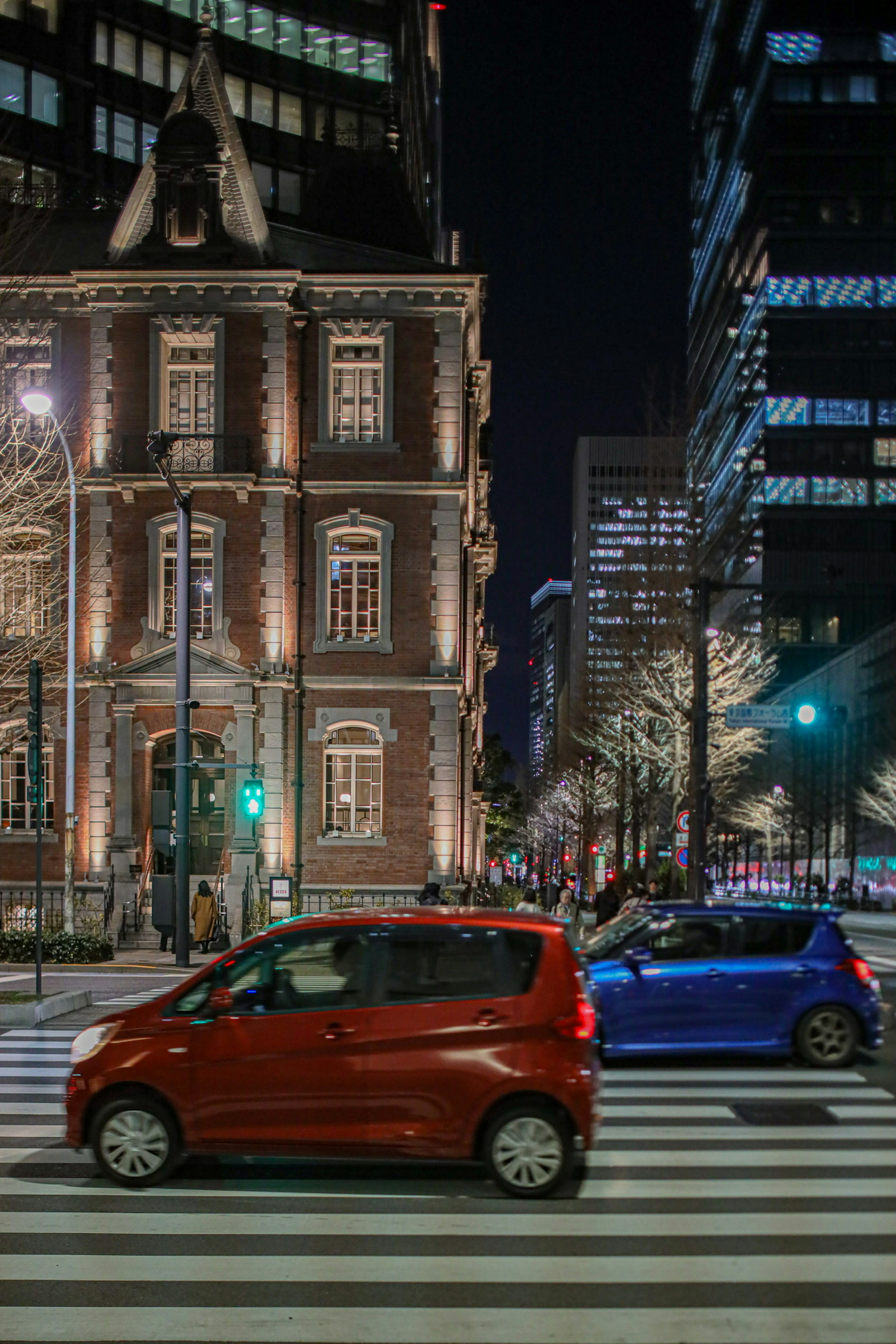 夜間紅色和藍色汽車穿越交叉路口，背景有歷史建築