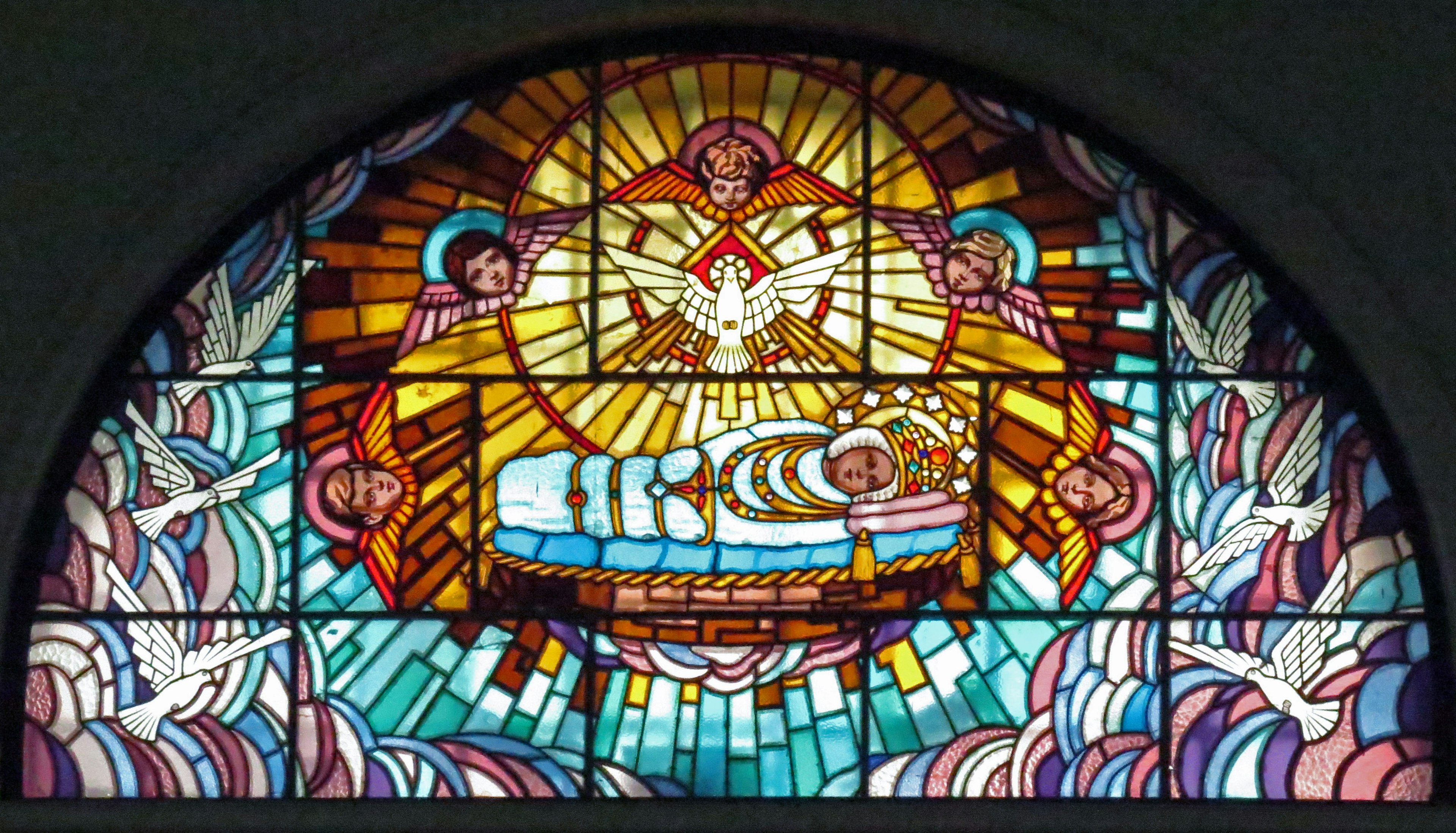 Stained glass depicting the Nativity scene with the Virgin Mary and baby Jesus surrounded by doves and rays of light