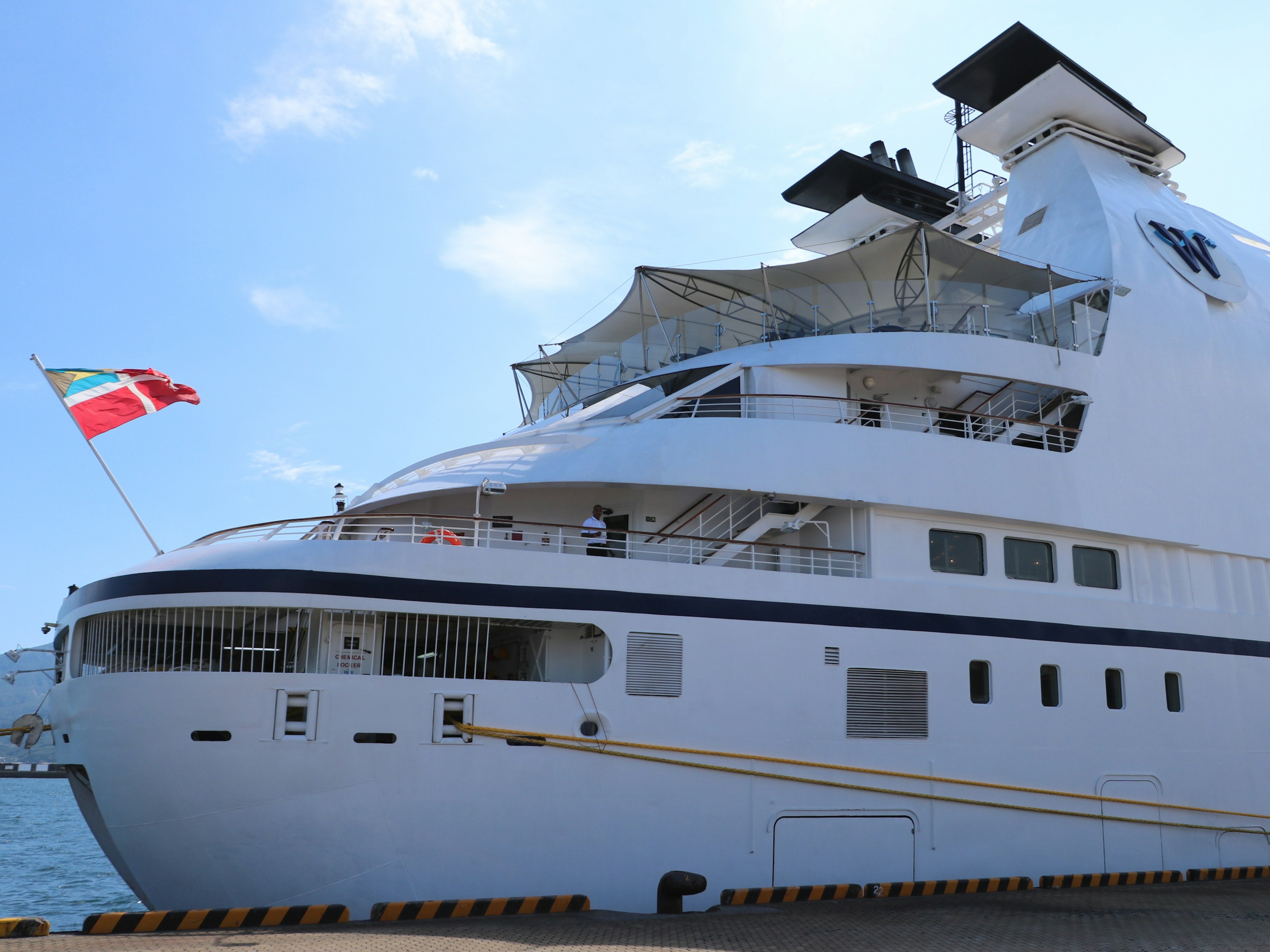 A large white cruise ship docked at a port featuring a national flag on its side