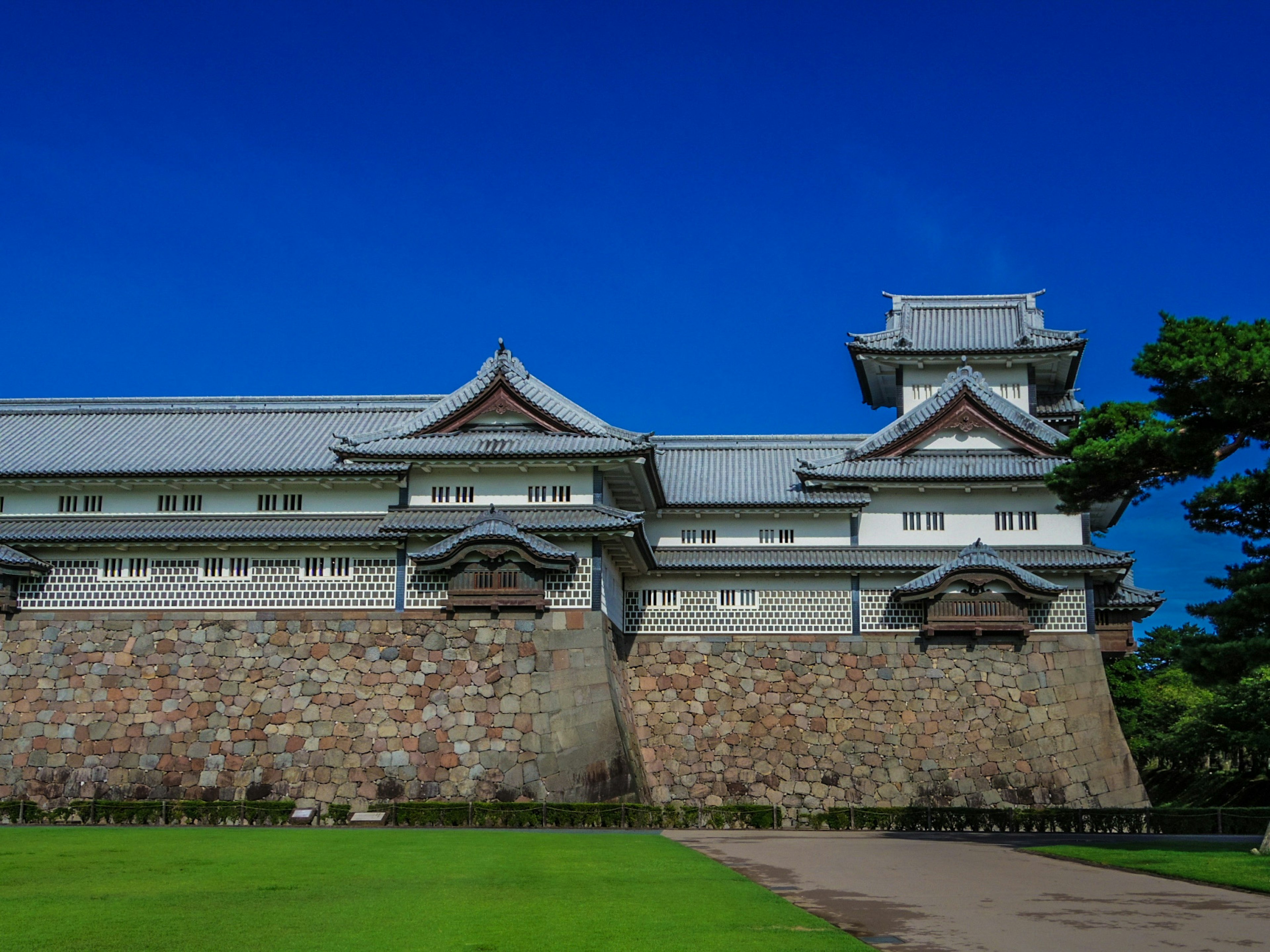 Extérieur d'un château japonais traditionnel sous un ciel bleu avec une base en pierre et un design de toit élégant